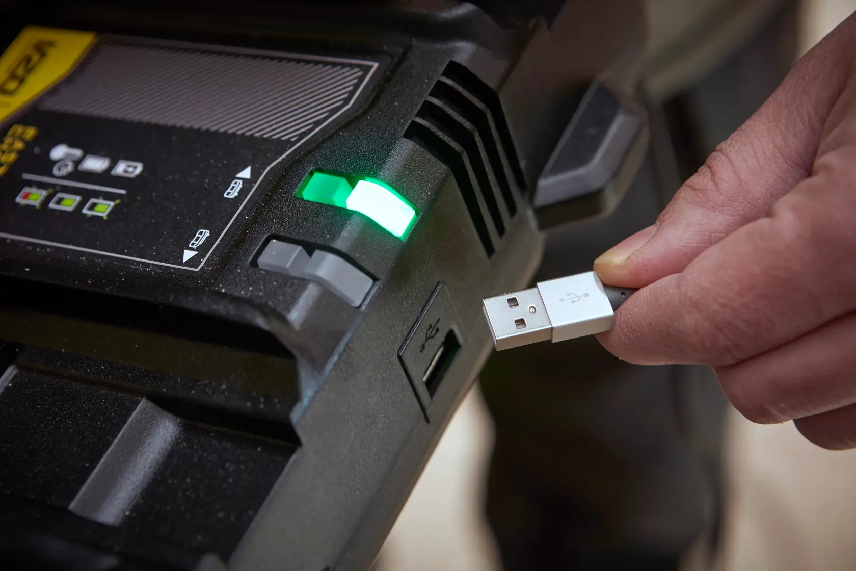 STANLEY SFMCB24 Akkuladegerät mit grünem Indikator und Person, die ein USB-Kabel einsteckt, Nahaufnahme.
