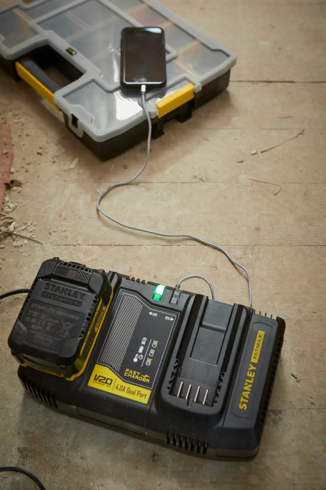 STANLEY SFMCB24 Doppelanschluss-Batterieladegerät lädt ein Gerät, Werkstattboden, angewinkelte Ansicht.