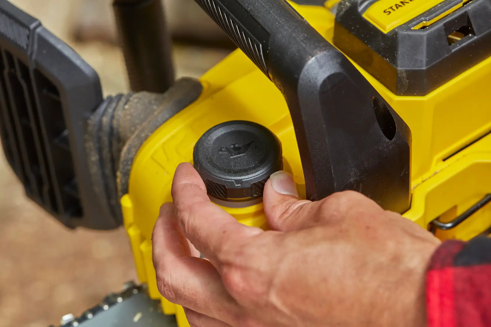 STANLEY SFMCCS630M1 Kettensäge Nahaufnahme, Hand am Öldeckel, gelb-schwarzes Design, Outdoor-Umgebung.