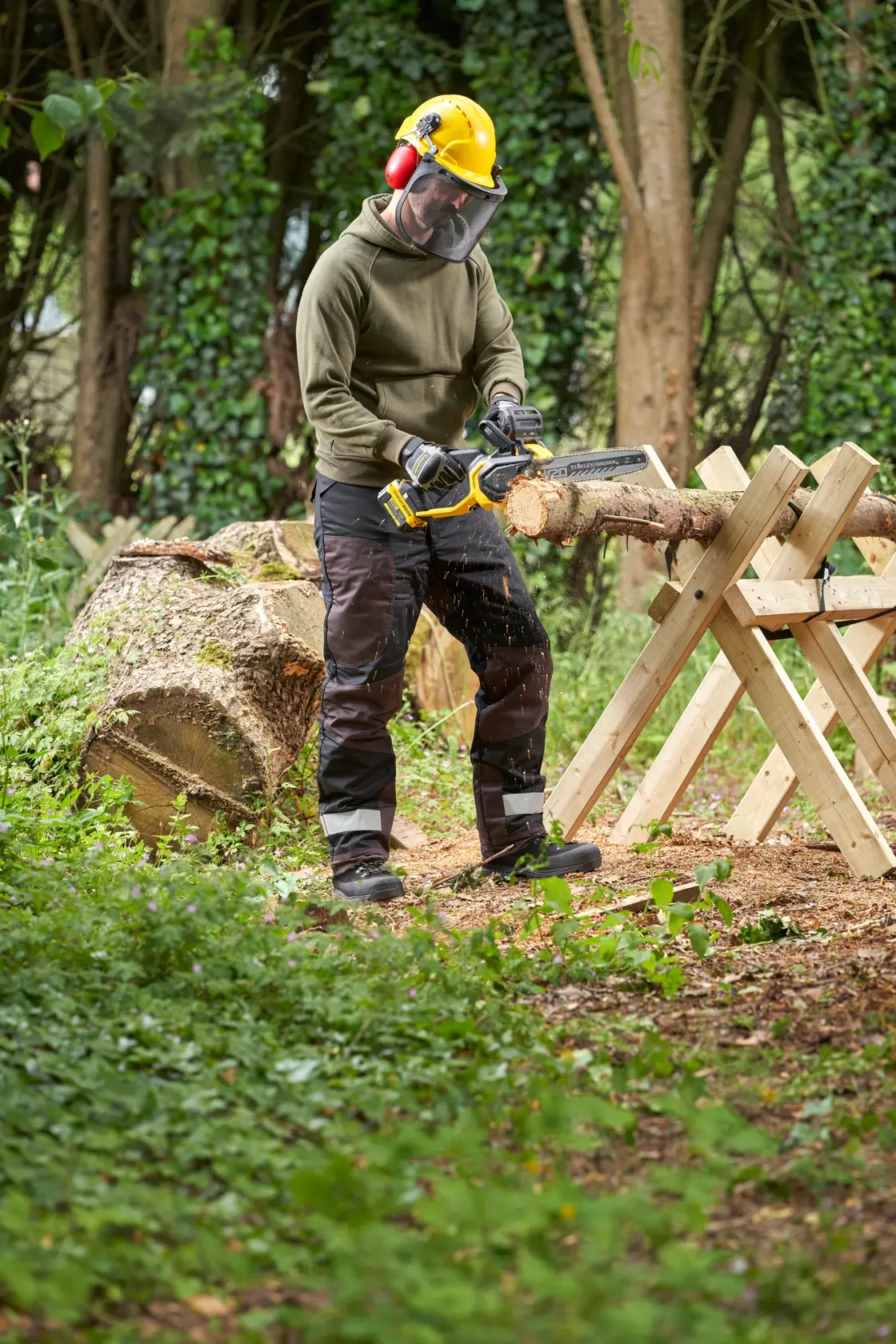 STANLEY SFMCCS730B Kettensäge im Einsatz beim Holzsägen im Freien, Bediener mit Schutzausrüstung, Waldumgebung.
