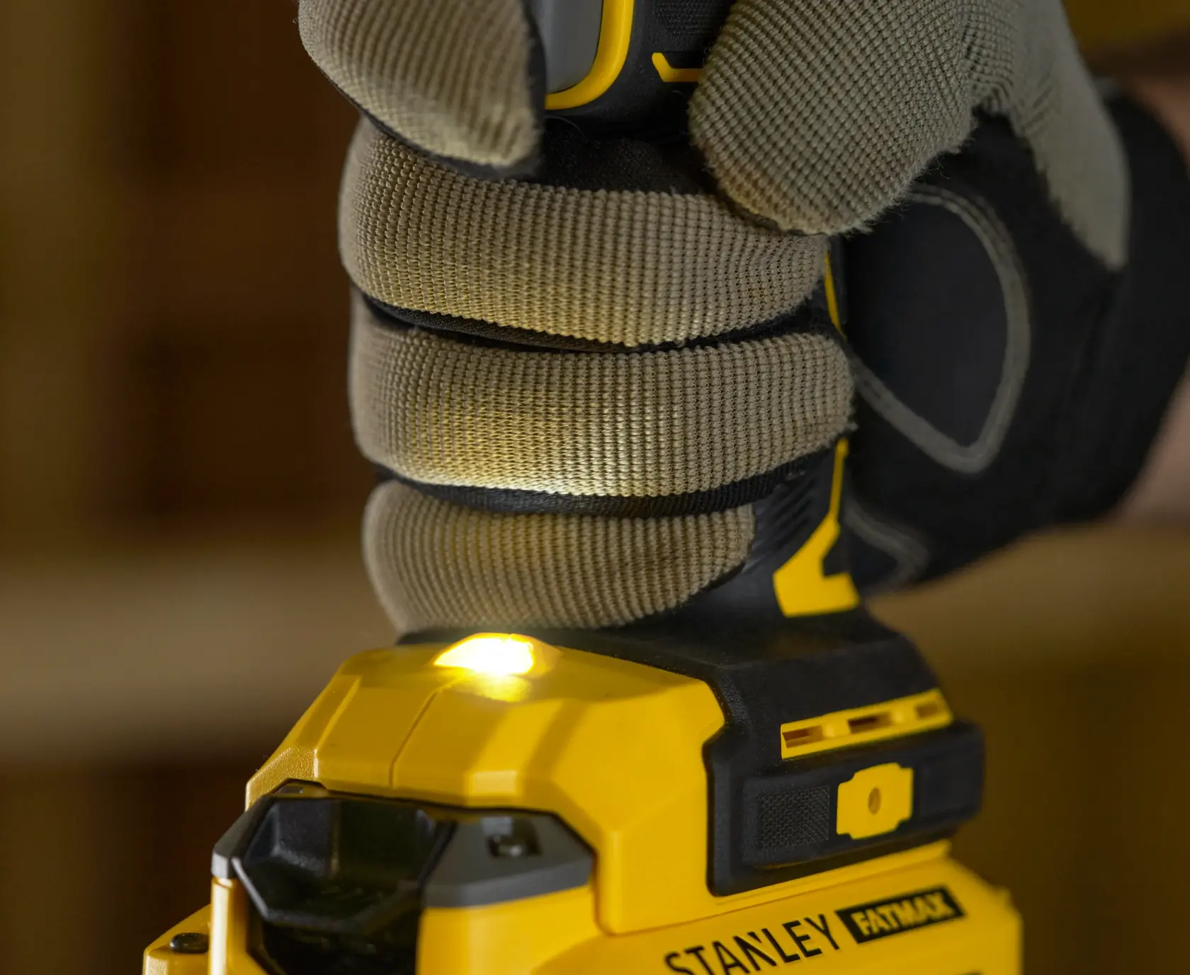 Foto einer behandschuhten Hand am STANLEY SFMCD720D2K Akku-Bohrschrauber mit eingeschaltetem LED-Licht, Nahaufnahme.