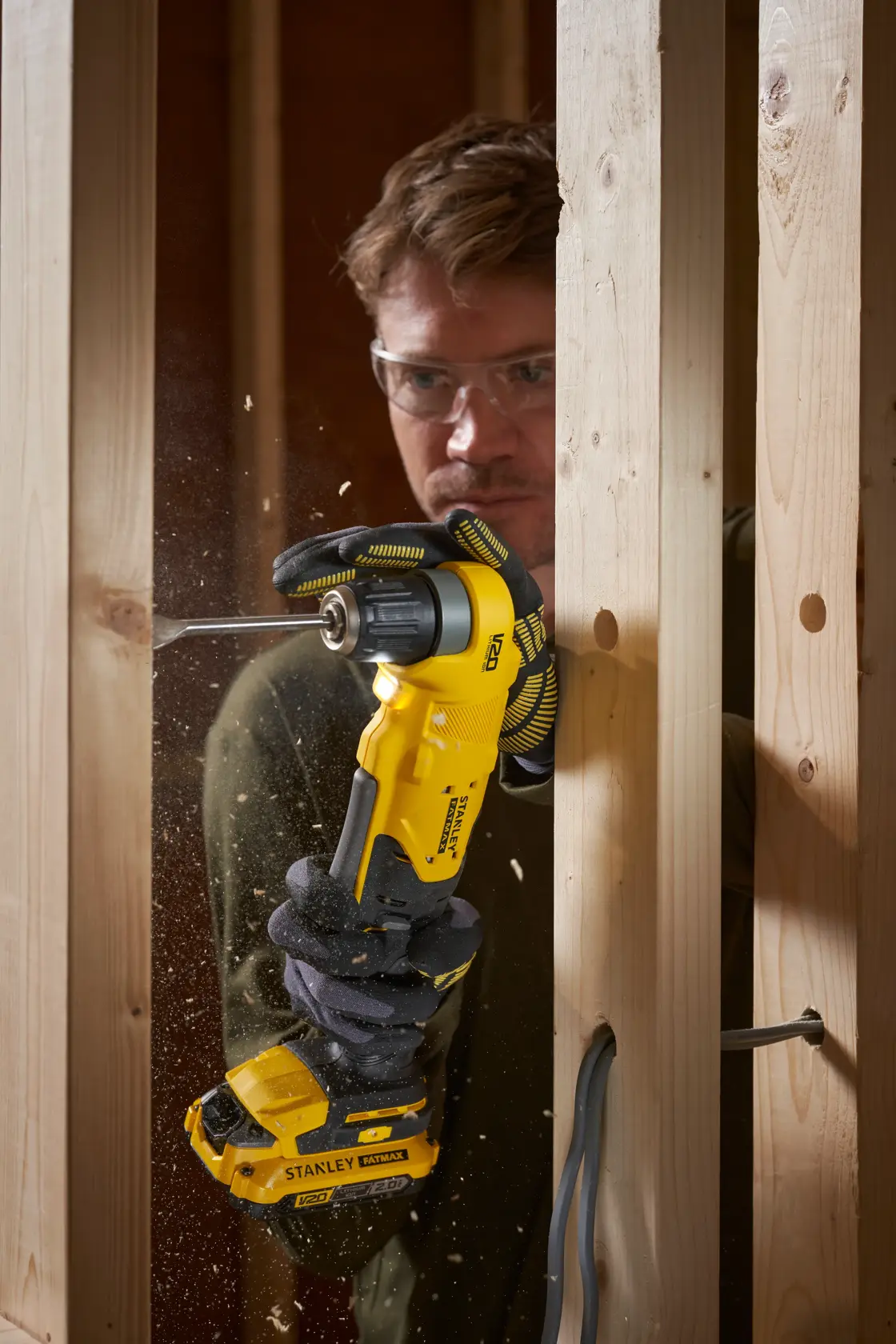 STANLEY SFMCD750B Akku-Winkelbohrmaschine im Einsatz beim Bohren durch Holzständer, Nahaufnahme in Aktion.