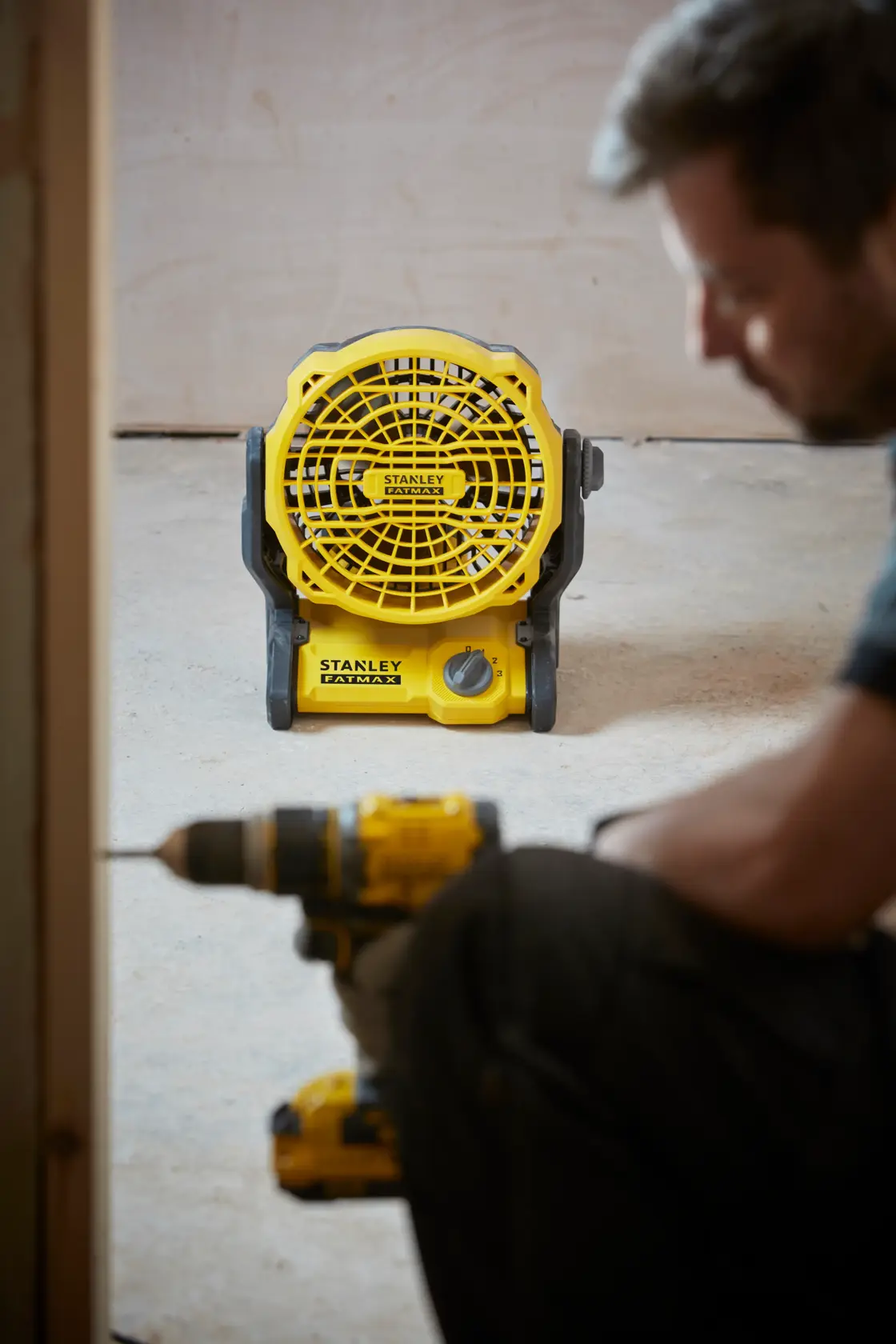 Foto des gelben tragbaren STANLEY SFMCE001B Ventilators auf dem Boden, mit Bauwerkzeug im Vordergrund.
