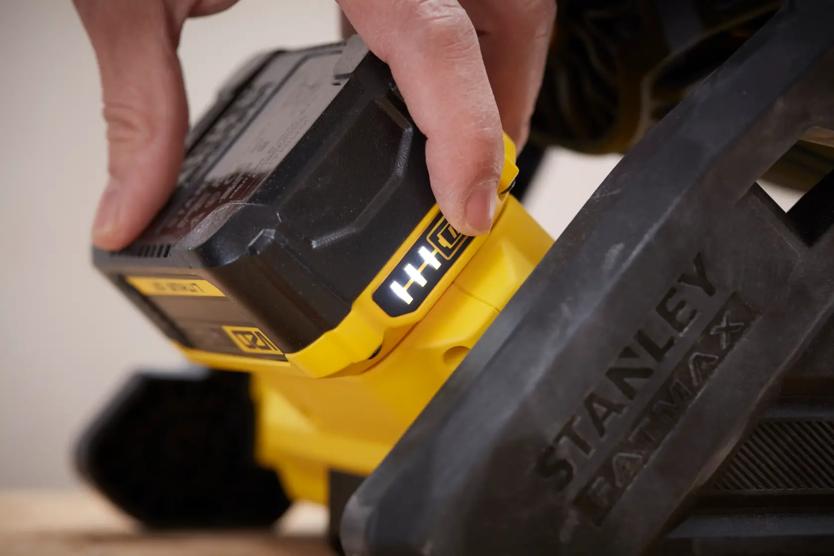 Nahaufnahme einer Hand, die den Akku in das STANLEY SFMCE001B Elektrowerkzeug einsetzt, mit gelben und schwarzen Details.