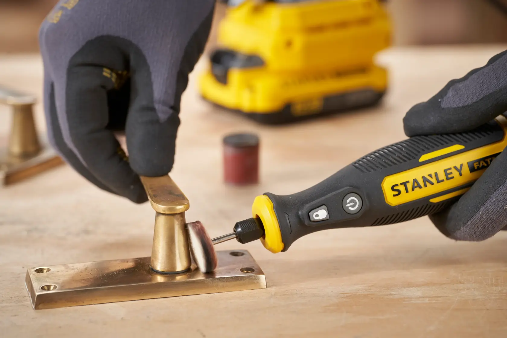 STANLEY SFMCE030B Rotationswerkzeug poliert Messing-Beschlag auf Holzoberfläche, Nahaufnahme.