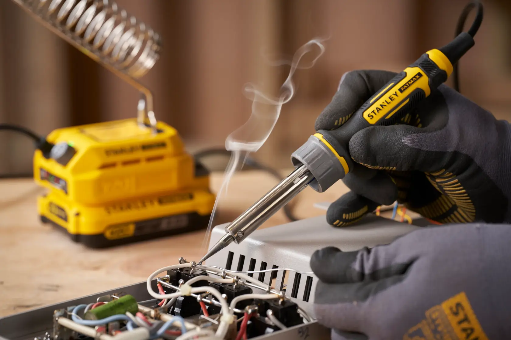 Foto des STANLEY SFMCE040B Lötkolbens im Einsatz, behandschuhte Hand lötet elektronische Bauteile auf eine Platine.
