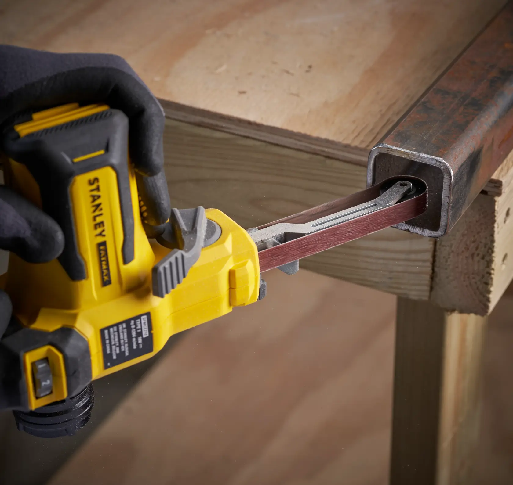 STANLEY SFMCE210B kabellose Bandschleife schleift das Innere eines Metallrohrs, Seitenansicht, gehalten mit Handschuh.