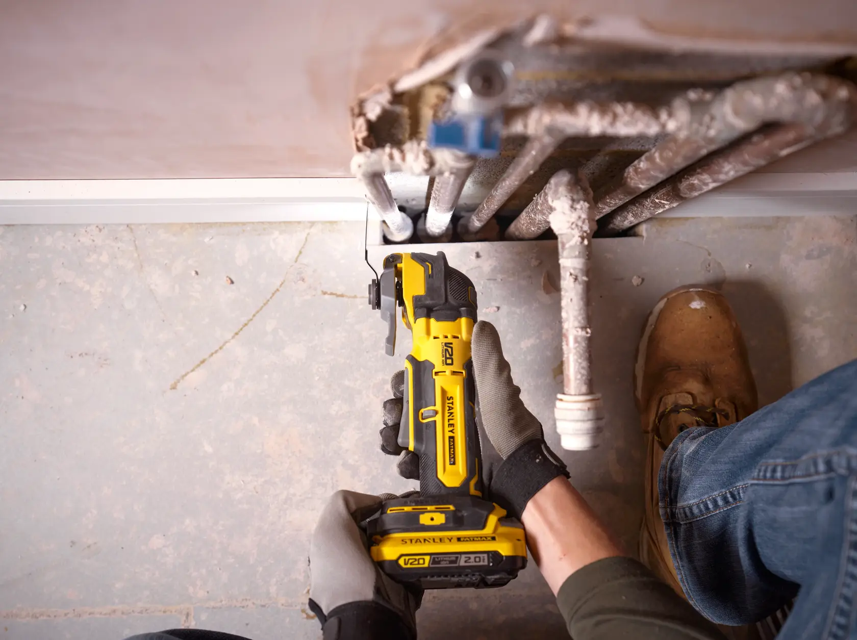 Foto des STANLEY SFMCE510B oszillierenden Multitools beim Schneiden neben Rohren auf Betonboden.