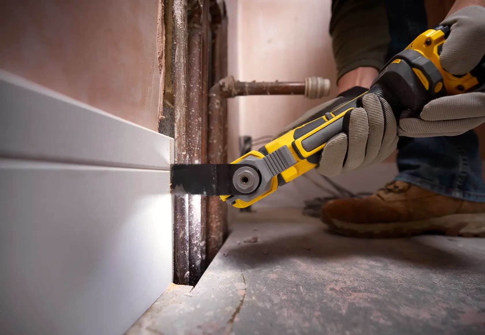 STANLEY SFMCE510B oszillierendes Multifunktionswerkzeug schneidet Sockelleiste nahe Rohren, Nahaufnahme bei Renovierung.