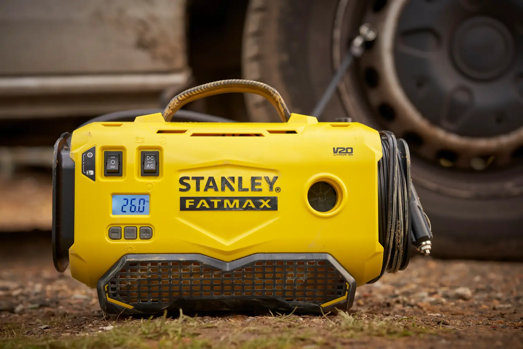 Foto des gelben STANLEY SFMCE520B FATMAX tragbaren Reifenfüllers mit Digitalanzeige und Schlauch, draußen.
