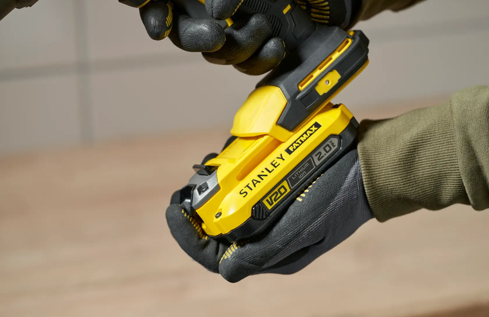 Foto vom gelben kabellosen Werkzeug STANLEY SFMCE600B in behandschuhten Händen, Seitenansicht Nahaufnahme.