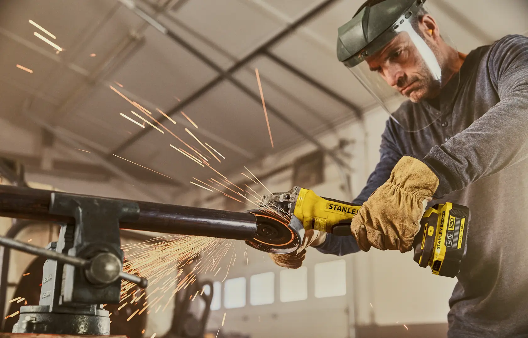 Foto der STANLEY SFMCG700B kabellosen Winkelschleifer beim Schneiden eines Metallrohrs mit Funken im Werkstatt.