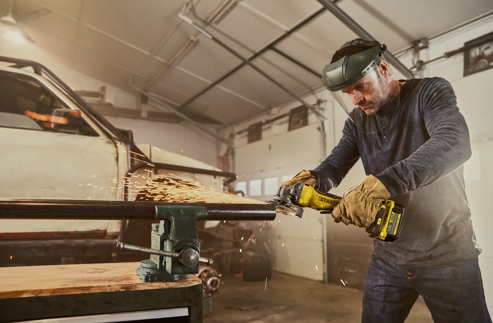 STANLEY SFMCG700B kabelloser Winkelschleifer im Einsatz, erzeugt Funken beim Schleifen eines Metallrohrs in Werkstatt.
