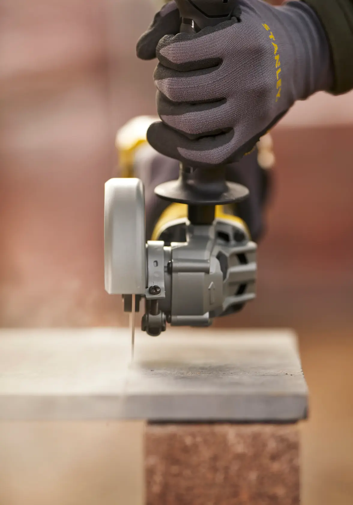 STANLEY SFMCG700M2K Schleifer schneidet Steinplatte, Winkelansicht, STANLEY Handschuhe getragen.