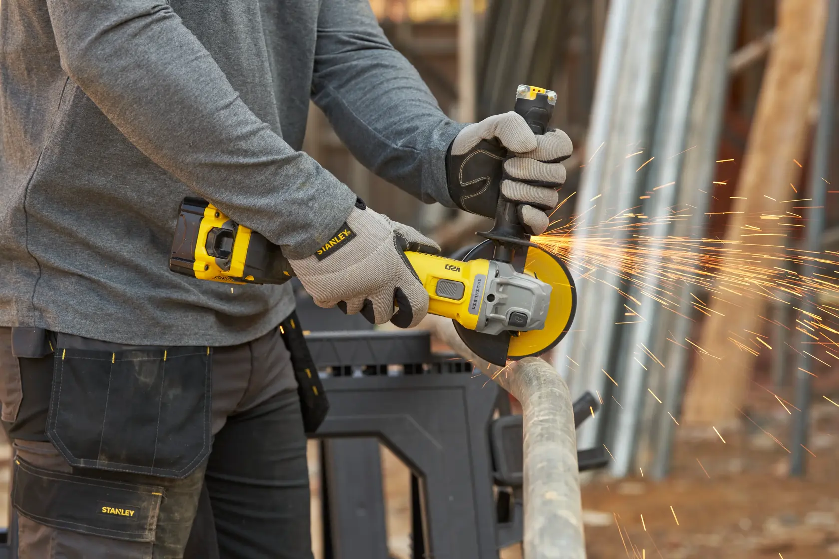 Stanley SFMCG710B-XJ kabelloser Winkelschleifer beim Schneiden eines Metallrohrs, gelb-schwarzes Werkzeug, Funken sichtbar.