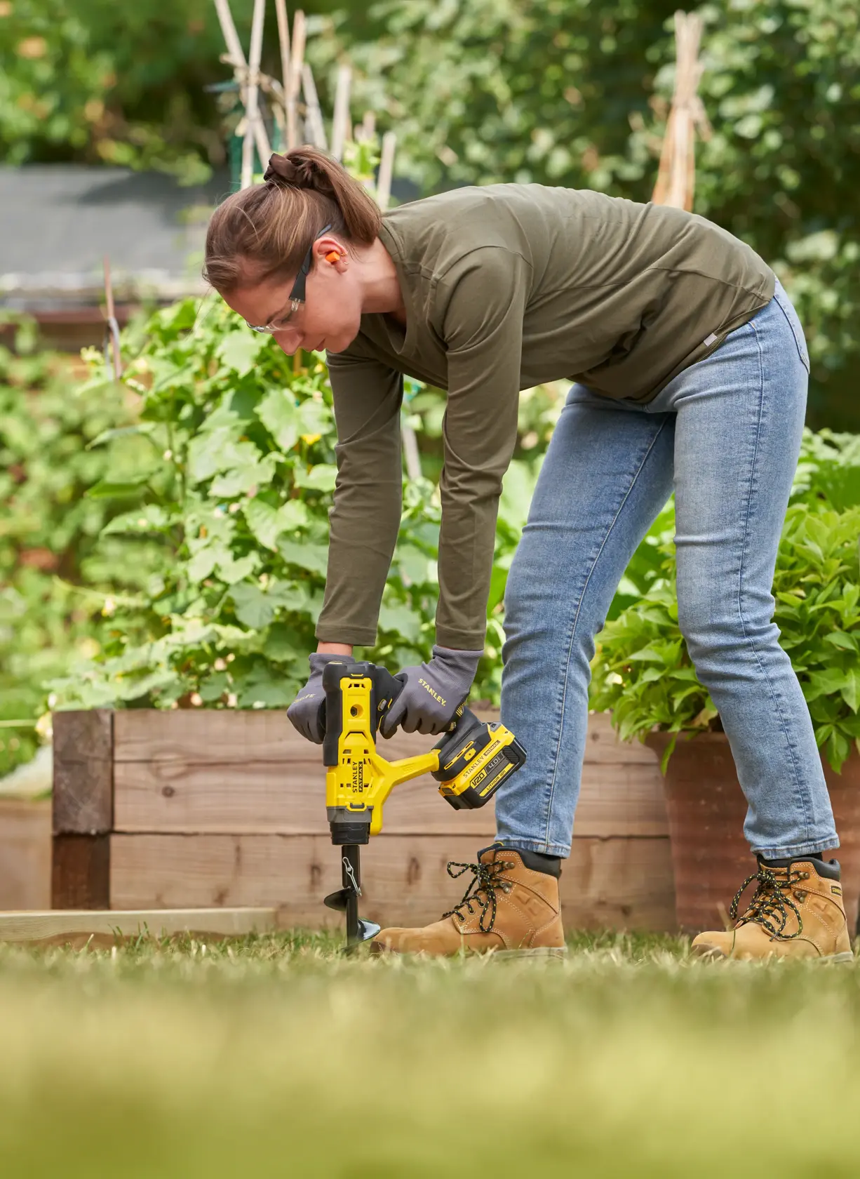 STANLEY SFMCGA75M1 kabelloser Gartenbohrer im Einsatz im Freien neben Hochbeeten.