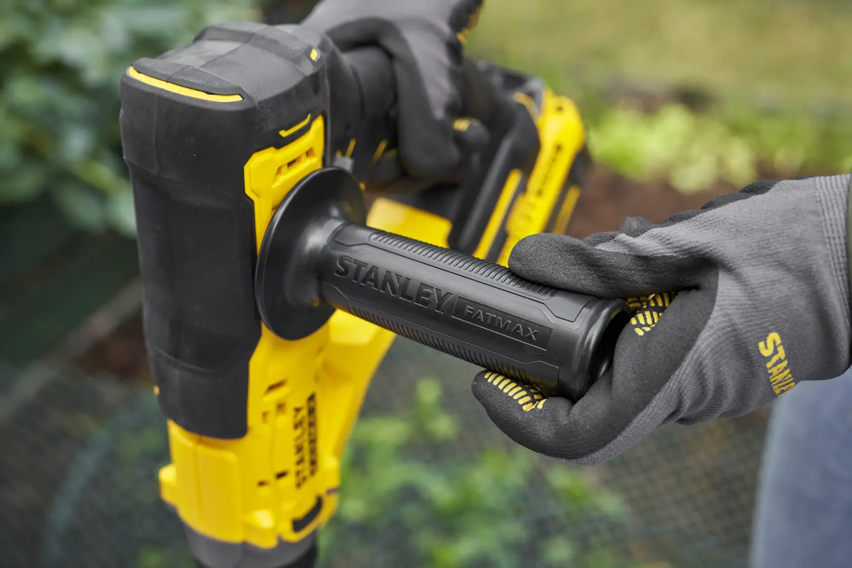 Foto des gelb-schwarzen Handgriffs des STANLEY SFMCGA75M1 Elektrowerkzeugs, gehalten von behandschuhten Händen im Freien.