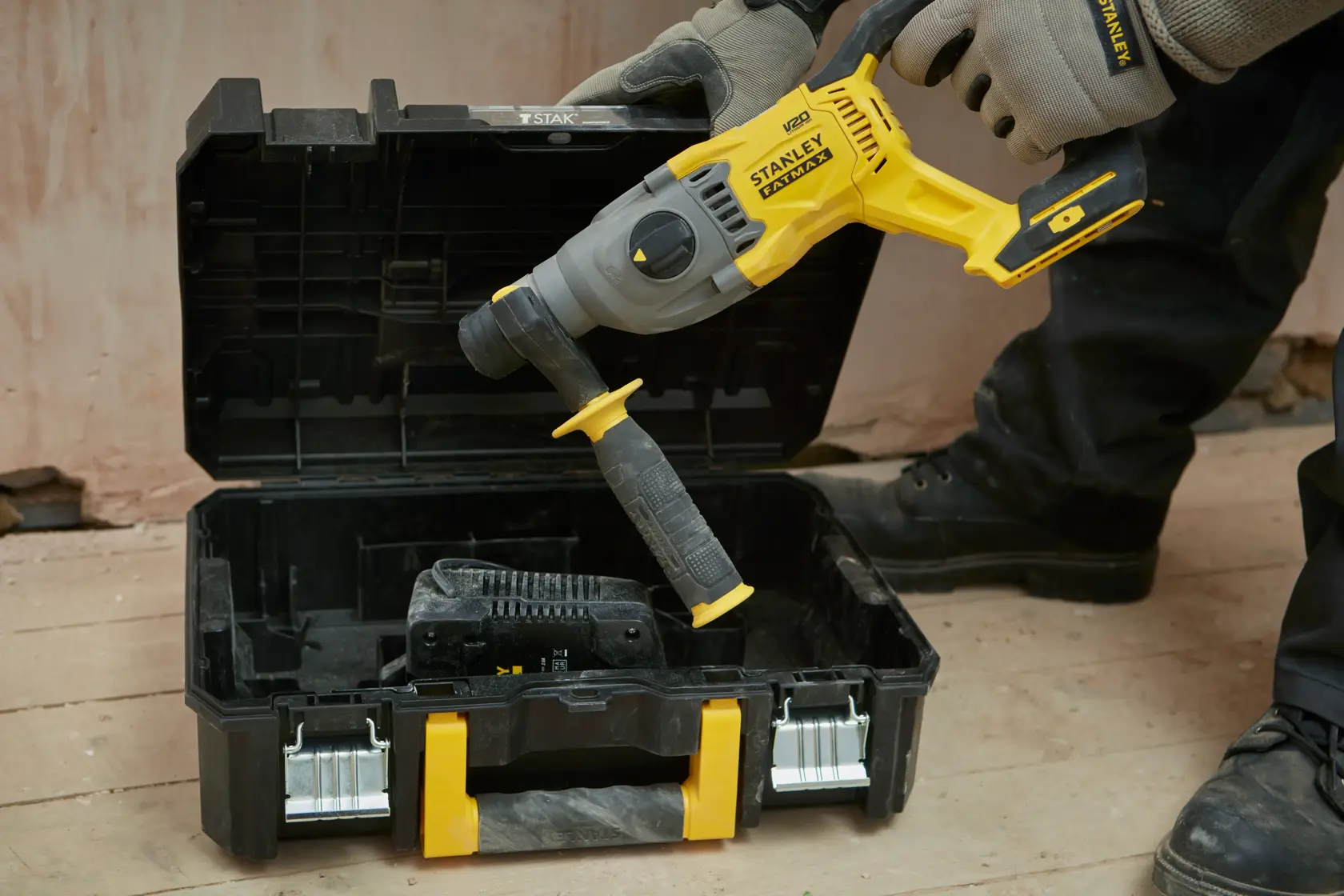 STANLEY SFMCH900B Bohrhammer wird in einen schwarz-gelben Transportkoffer auf dem Werkstattboden gelegt.
