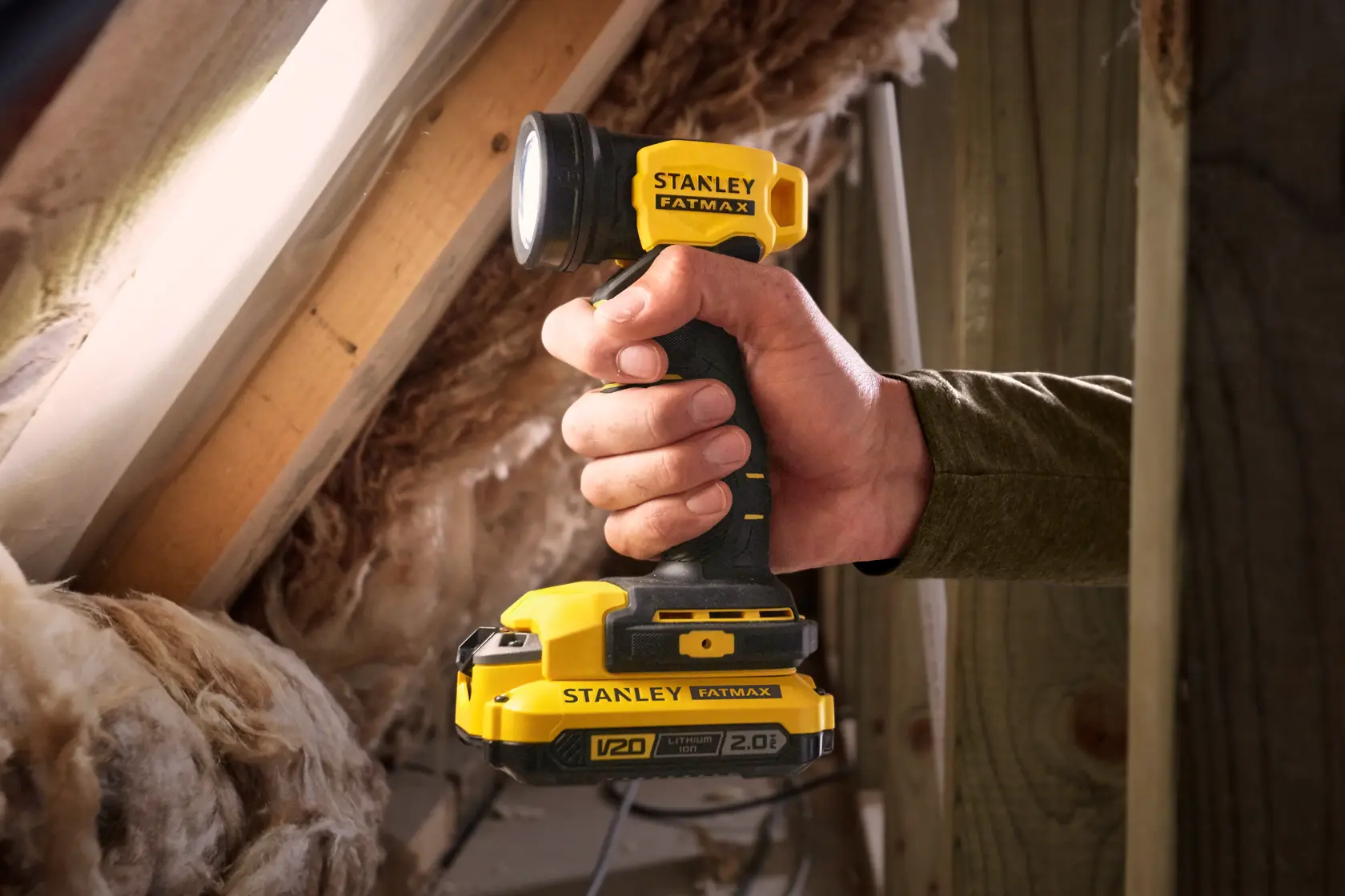 Foto der kabellosen gelb-schwarzen STANLEY SFMCL020B Arbeitsleuchte, in der Hand gehalten, im Dachboden.