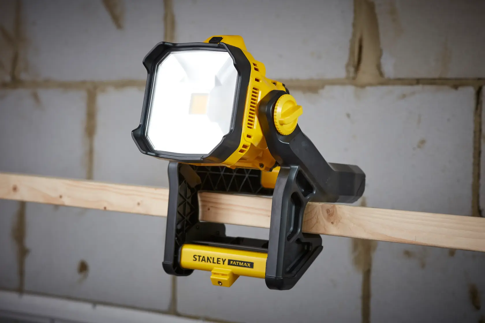 STANLEY SFMCL030B gelb-schwarzes LED-Arbeitslicht an Holzträger geklemmt, von vorne gezeigt.