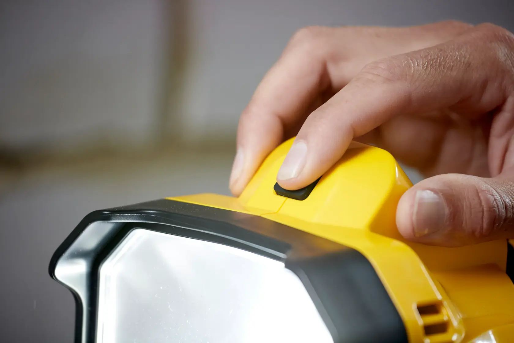 STANLEY SFMCL030B LED-Arbeitsleuchte Nahaufnahme, Finger drückt Netzschalter, gelbes und schwarzes Gehäuse.