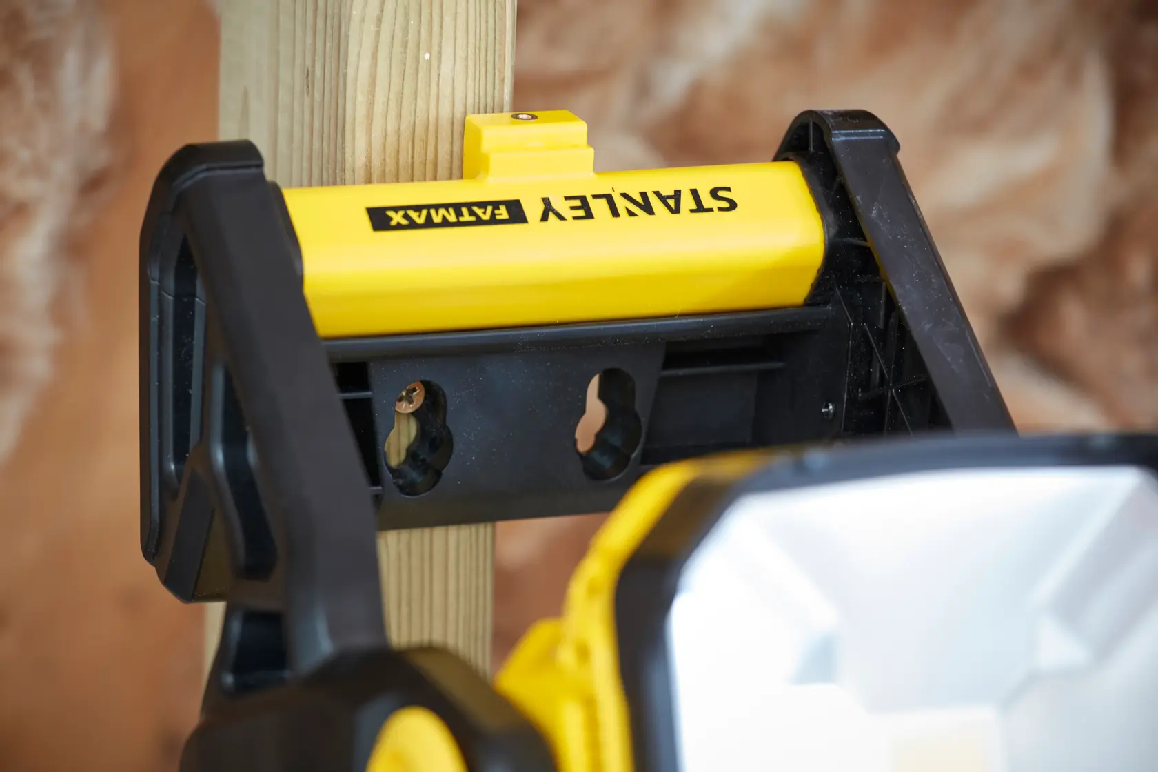 STANLEY SFMCL030B Arbeitsleuchte an Holzpfosten montiert, Nahaufnahme, gelb-schwarzes Gehäuse.