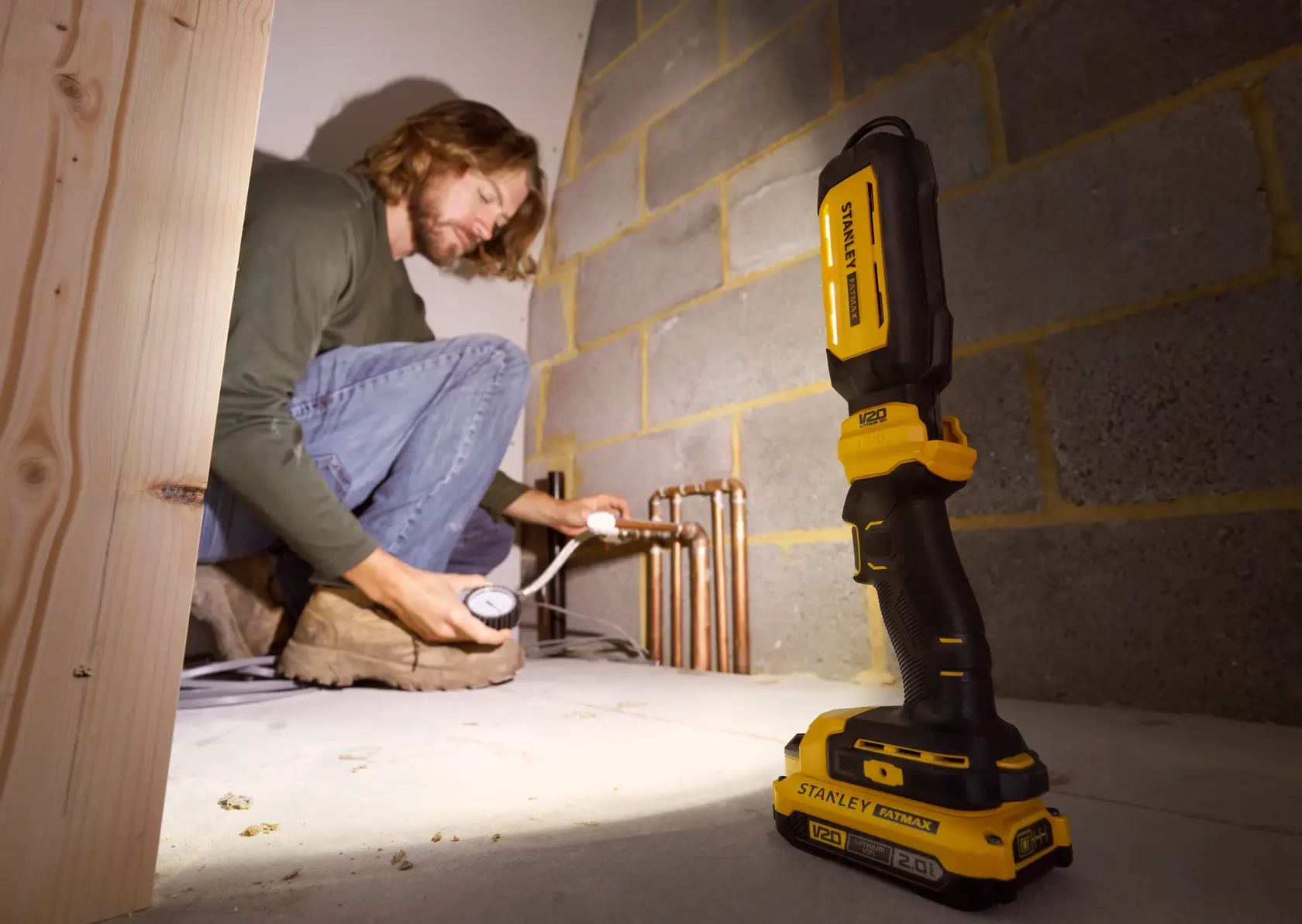 STANLEY SFMCL050B 18V FATMAX V20 Pivot Light auf dem Boden, beleuchtet Rohre, Person arbeitet im Hintergrund.