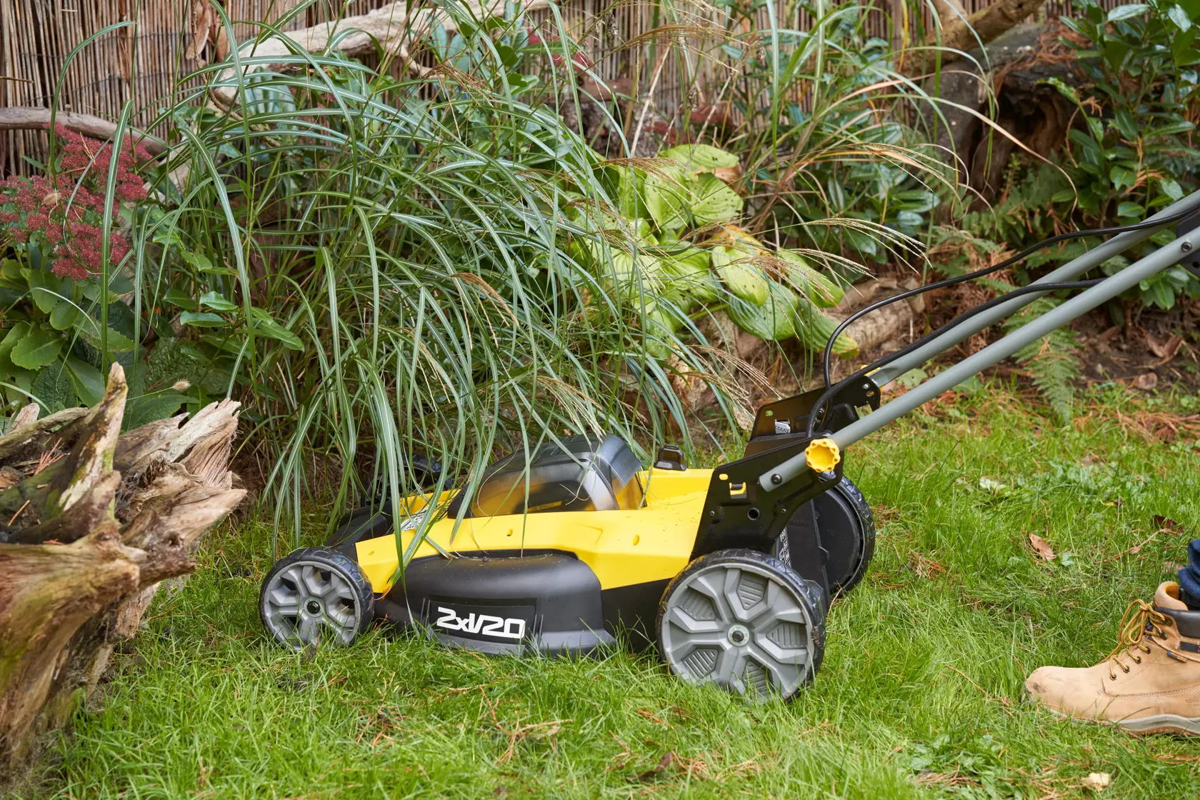 STANLEY SFMCMWS251M Rasenmäher Seitenansicht beim Mähen von Gras neben Pflanzen im Freien.