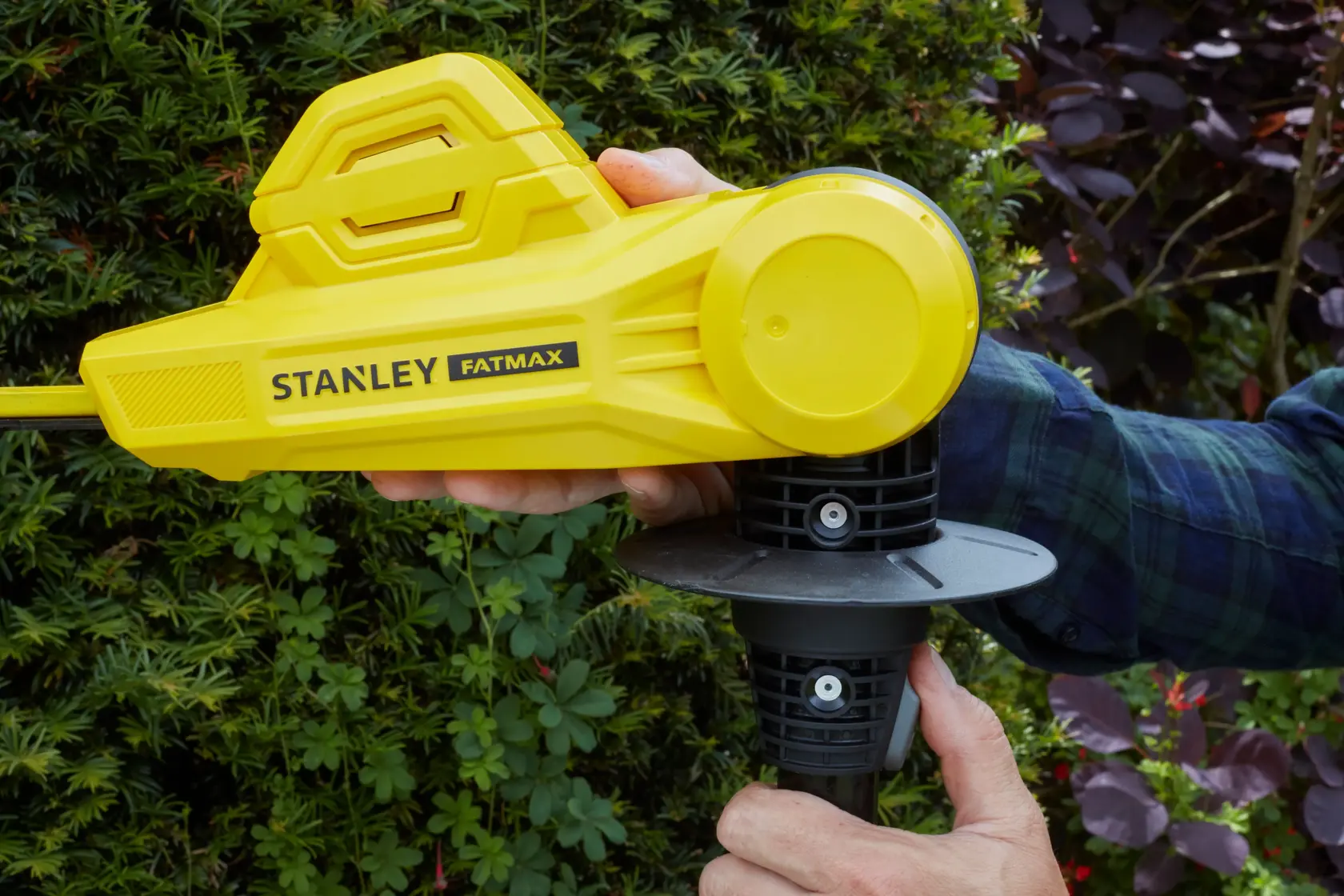 STANLEY SFMCPH845B gelbe Heckenschere Seitenansicht in Benutzung, Nahaufnahme mit Hand am Griff im Freien.