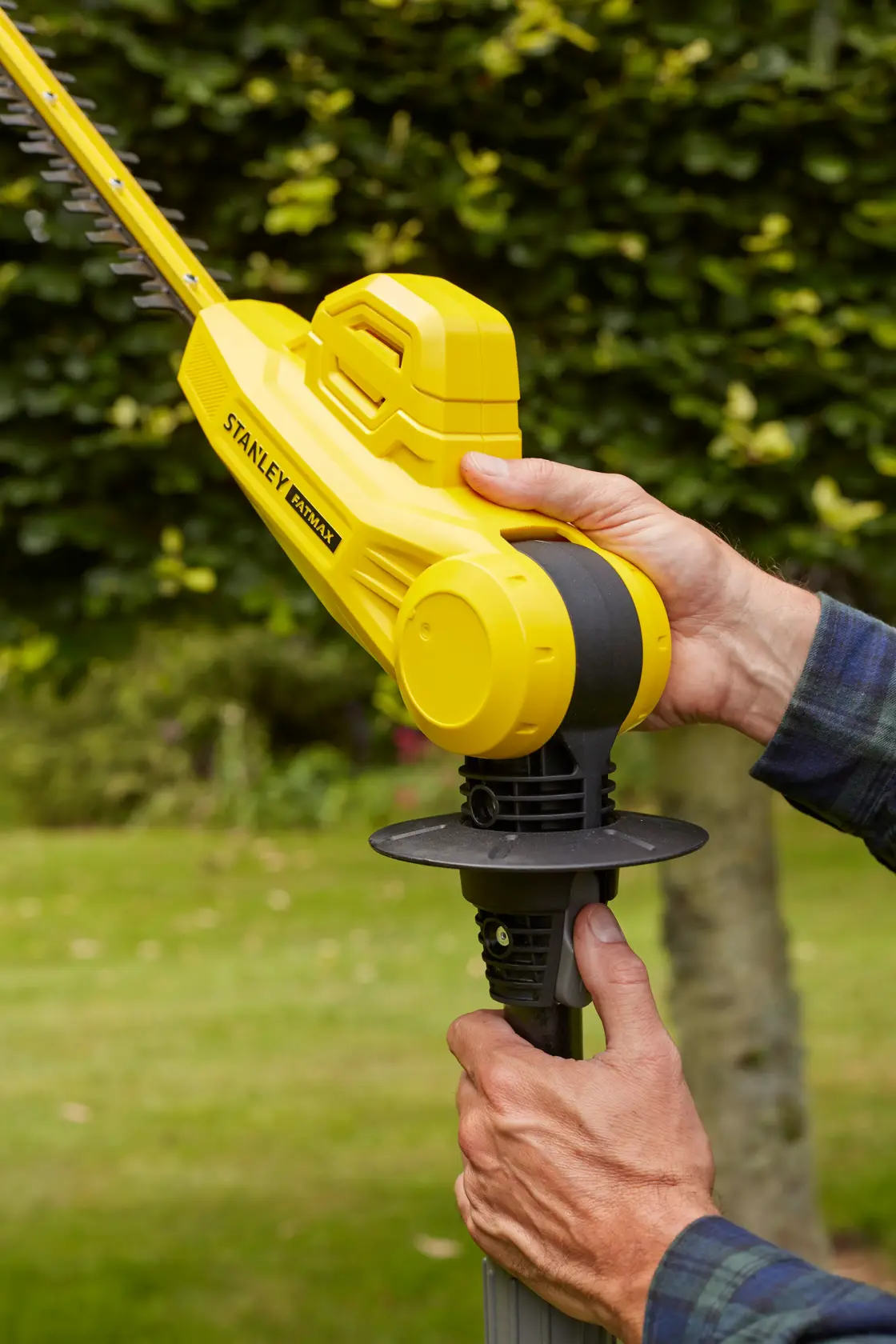 Foto des gelben kabellosen Heckenschneiders STANLEY SFMCPH845M1, der im Garten gehalten wird.