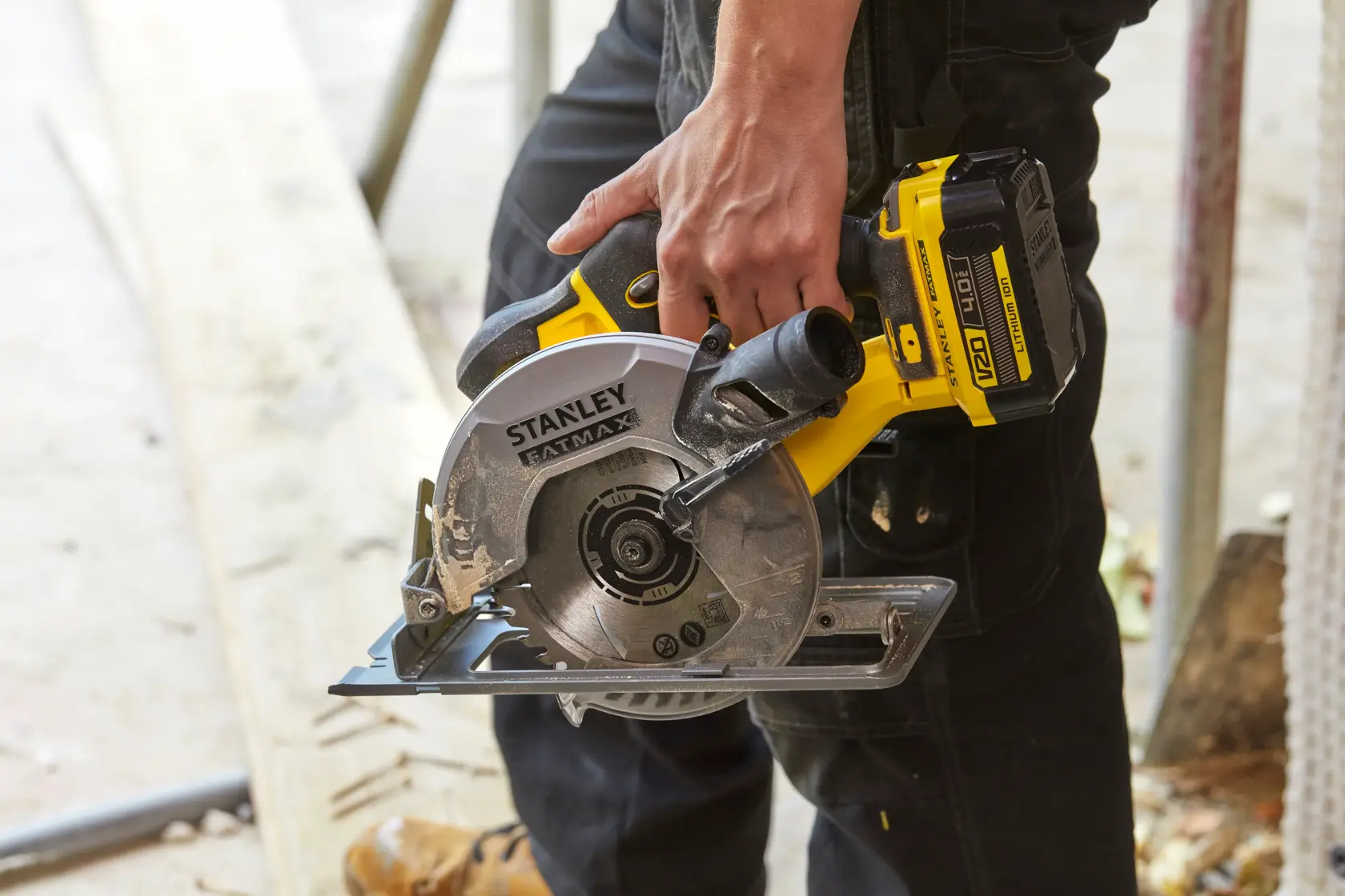 STANLEY SFMCS500B kabellose Kreissäge in gelb-schwarz von Person gehalten, Baustellenumgebung.