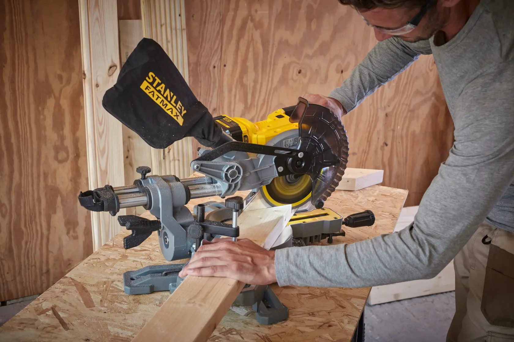 STANLEY SFMCS701M1 Kapp- und Gehrungssäge im Einsatz schneidet Holz auf Werkbank, Staubbeutel befestigt, Innenbereich.