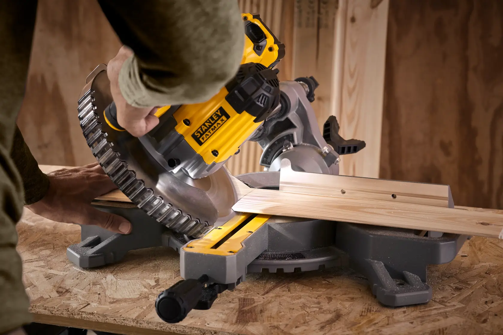 STANLEY SFMCS701M1 Gehrungssäge schneidet Holz, Nahaufnahme in schrägem Winkel, gelbes und schwarzes Werkzeug auf Werkbank.