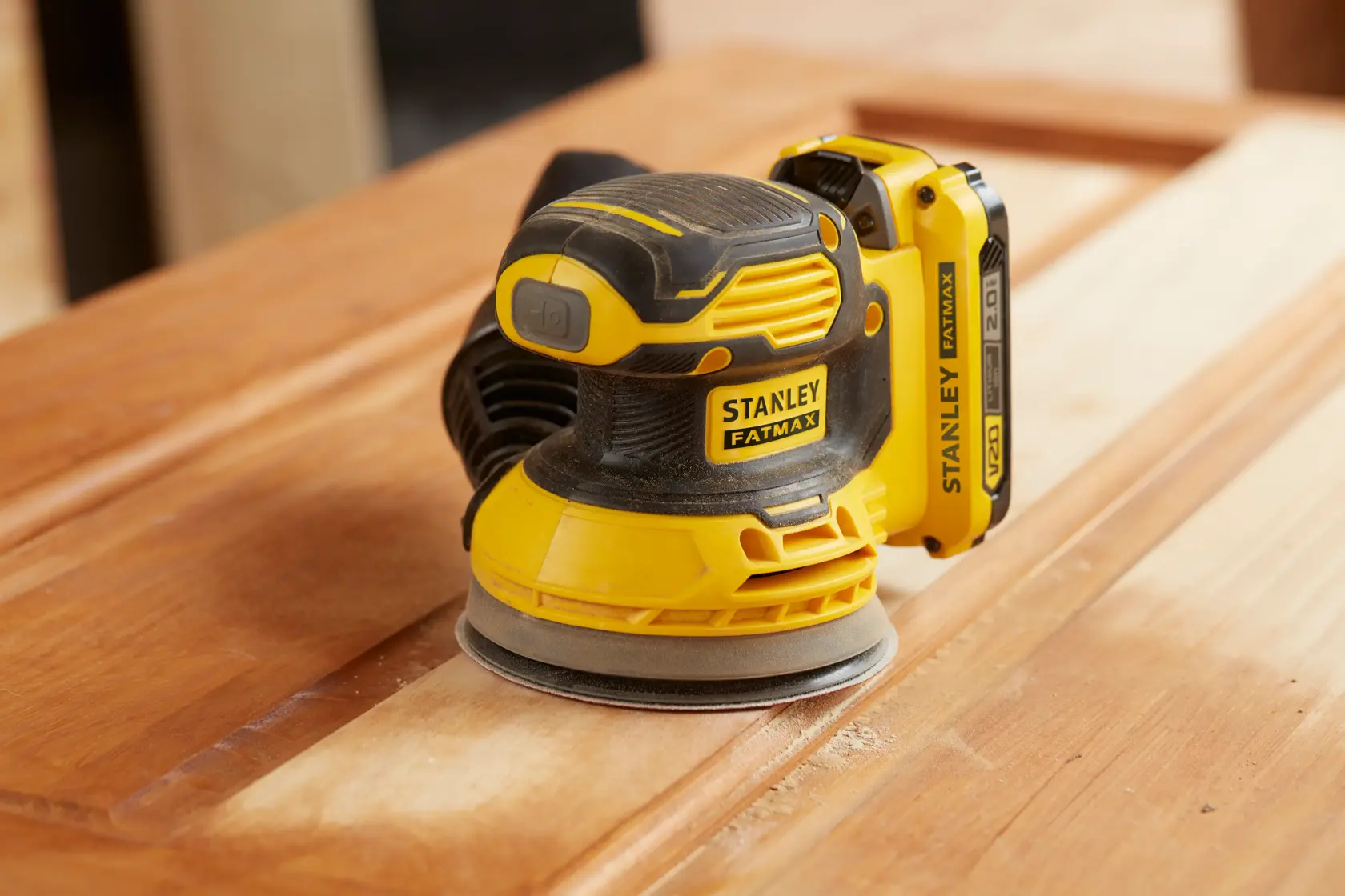 STANLEY SFMCW220D1S kabelloser gelb-schwarzer Exzenterschleifer, schleift eine Holzoberfläche.
