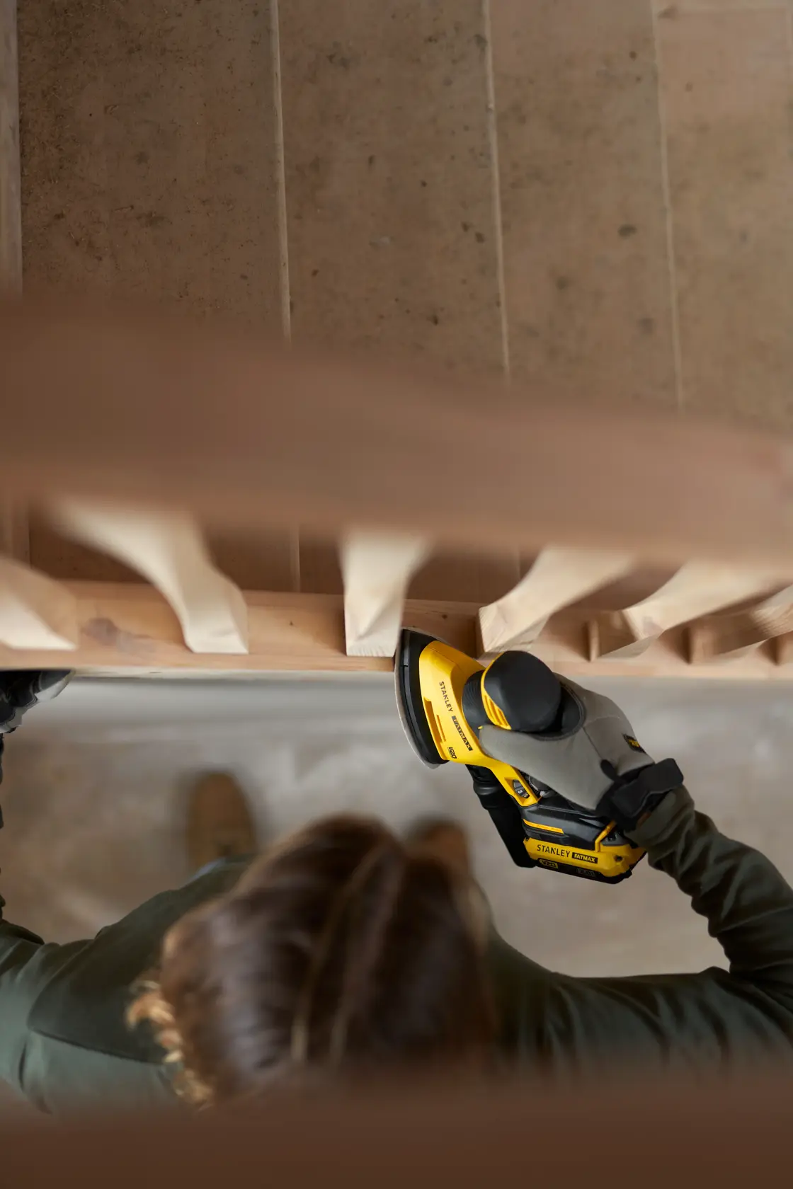Foto der STANLEY SFMCW221B Schleifmaschine im Einsatz an einem Holztreppengeländer, Hand hält das Werkzeug.