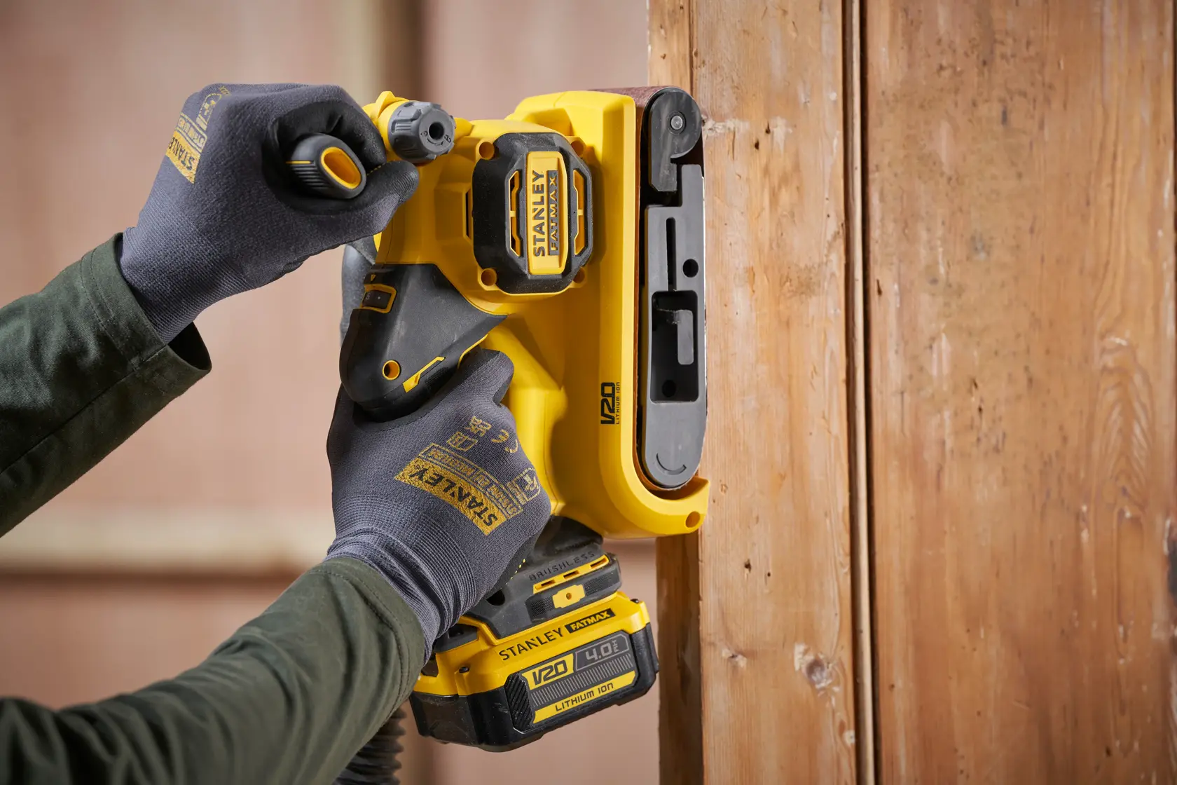 STANLEY SFMCW223B-XJ Akku-Schleifer im Einsatz an Holz, Nahaufnahme des gelben Werkzeugs in behandschuhter Hand.