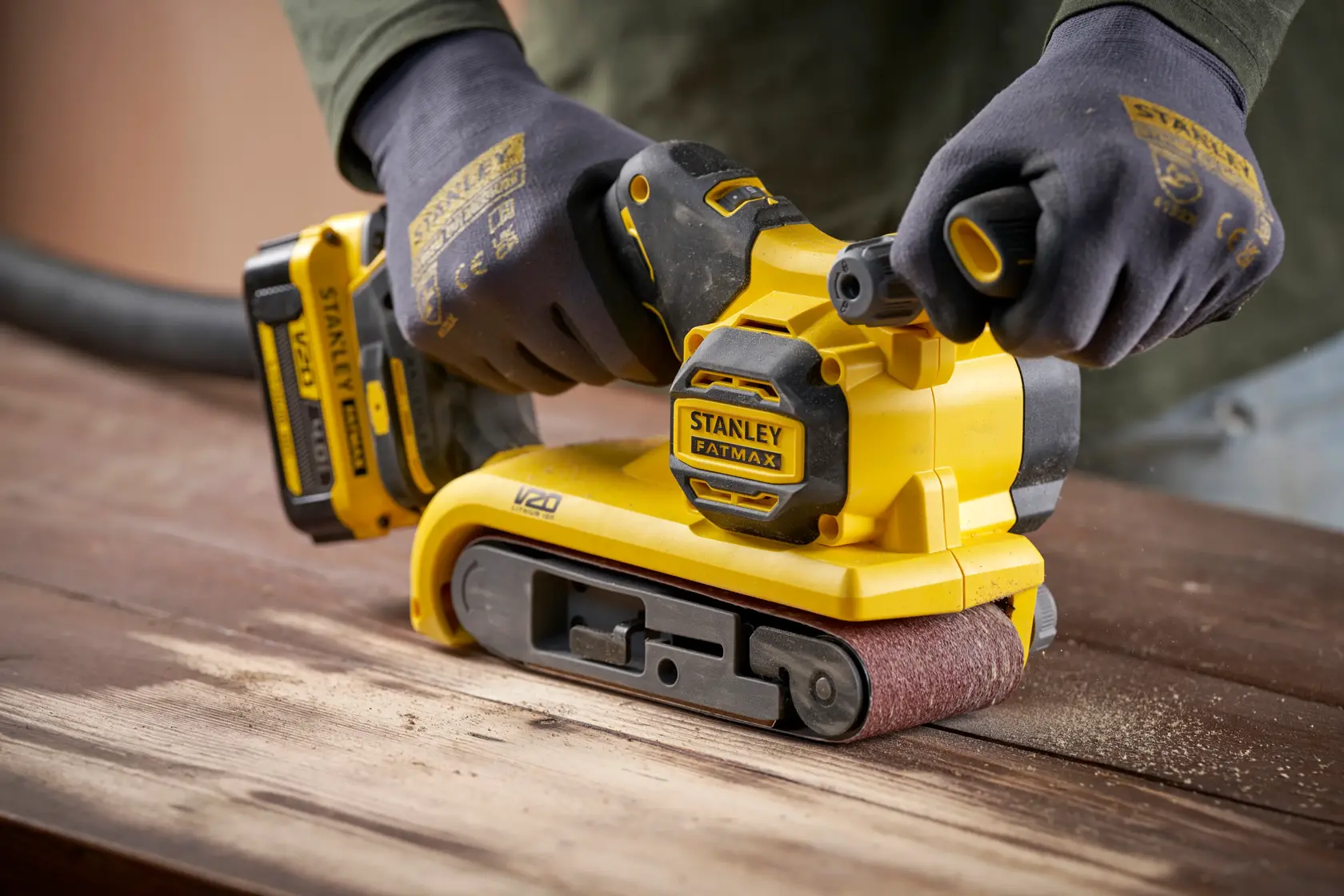 Stanley SFMCW223B-XJ kabelloser Bandschleifer auf Holz im Einsatz, Nahaufnahme, gelb und schwarz.