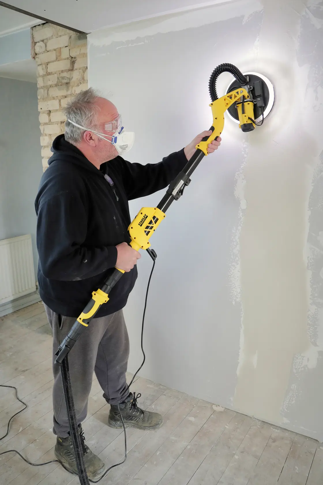 STANLEY SFMEE500S Trockenbauschleifer im Einsatz an einer Wand, seitliche Ansicht im Innenbereich.
