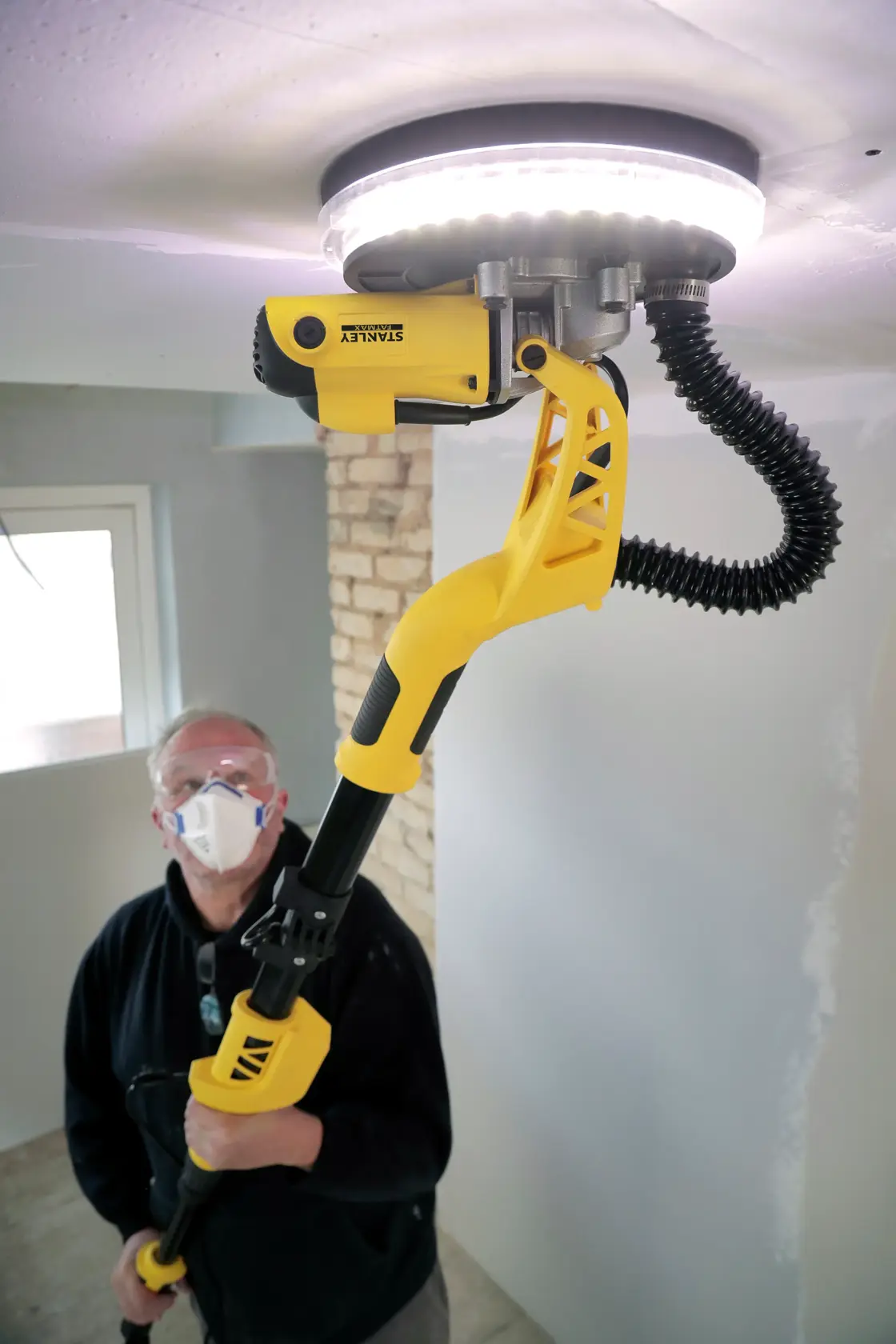 STANLEY SFMEE500S Trockenbauschleifer im Einsatz, gelb-schwarzes Werkzeug mit LED-Licht, schleift eine Decke.