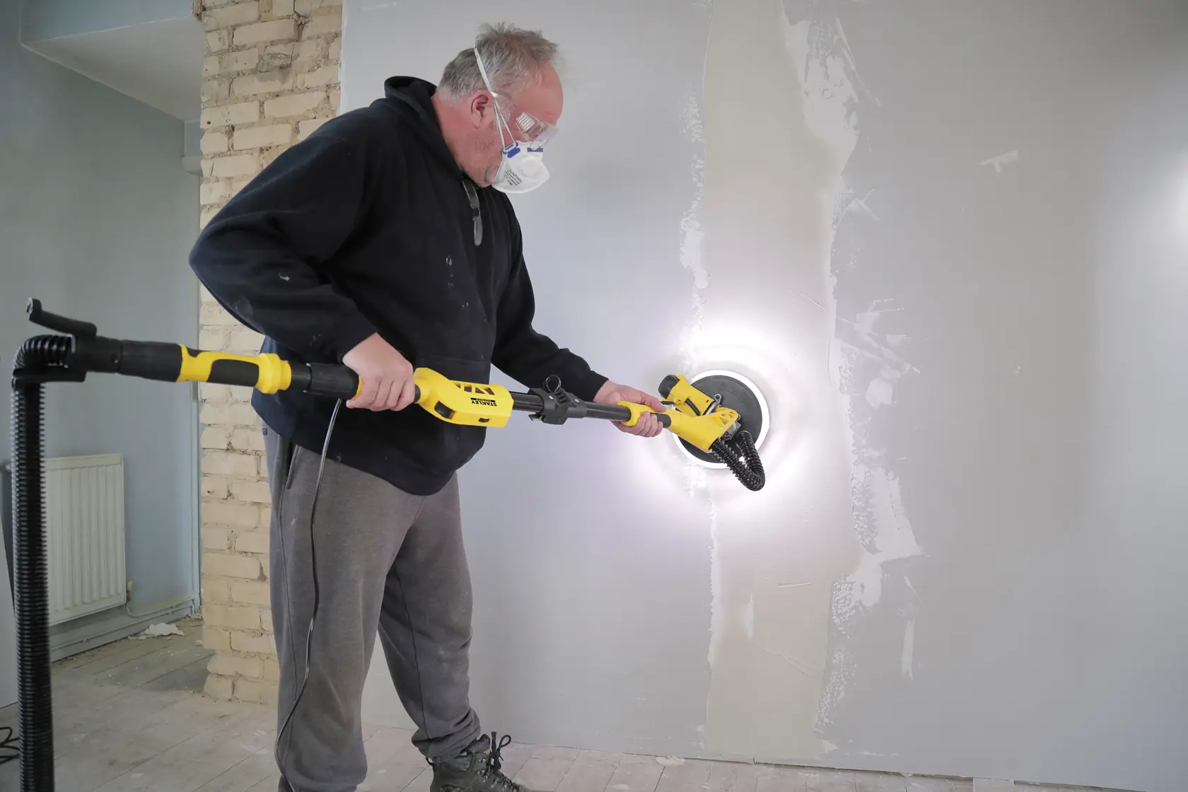 Foto von STANLEY SFMEE500S Trockenbauschleifer im Einsatz an einer Wand während Renovierung, Seitenansicht.
