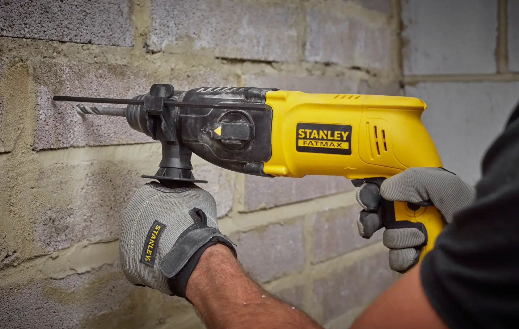 STANLEY SFMEH200K Bohrhammer im Einsatz an einer Mauer, gelb und schwarz, Nahaufnahme.