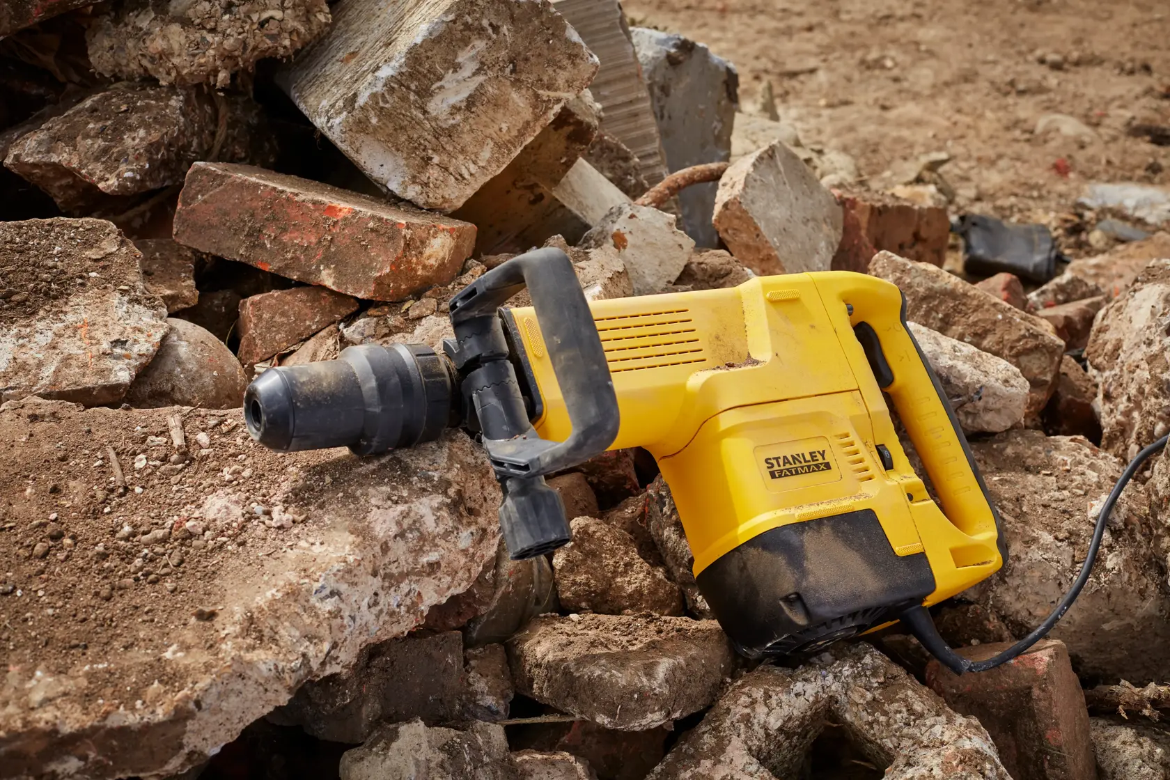 STANLEY SFMEH230K-QS Abbruchhammer auf Schutt, gelbes Gehäuse mit schwarzem Griff, Seitenansicht.