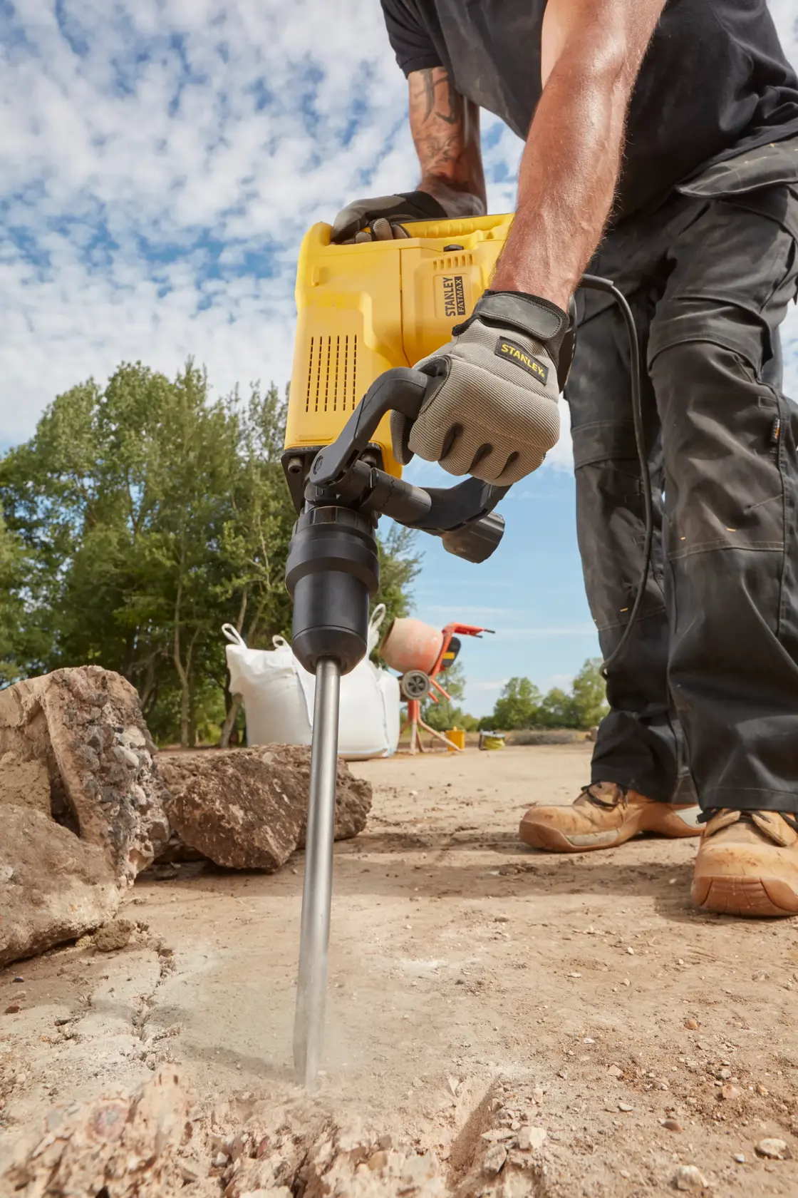 STANLEY SFMEH230K-QS Abbruchhammer im Einsatz beim Aufbrechen von Beton im Freien, Nahaufnahme von Werkzeug und Arbeiterhänden.