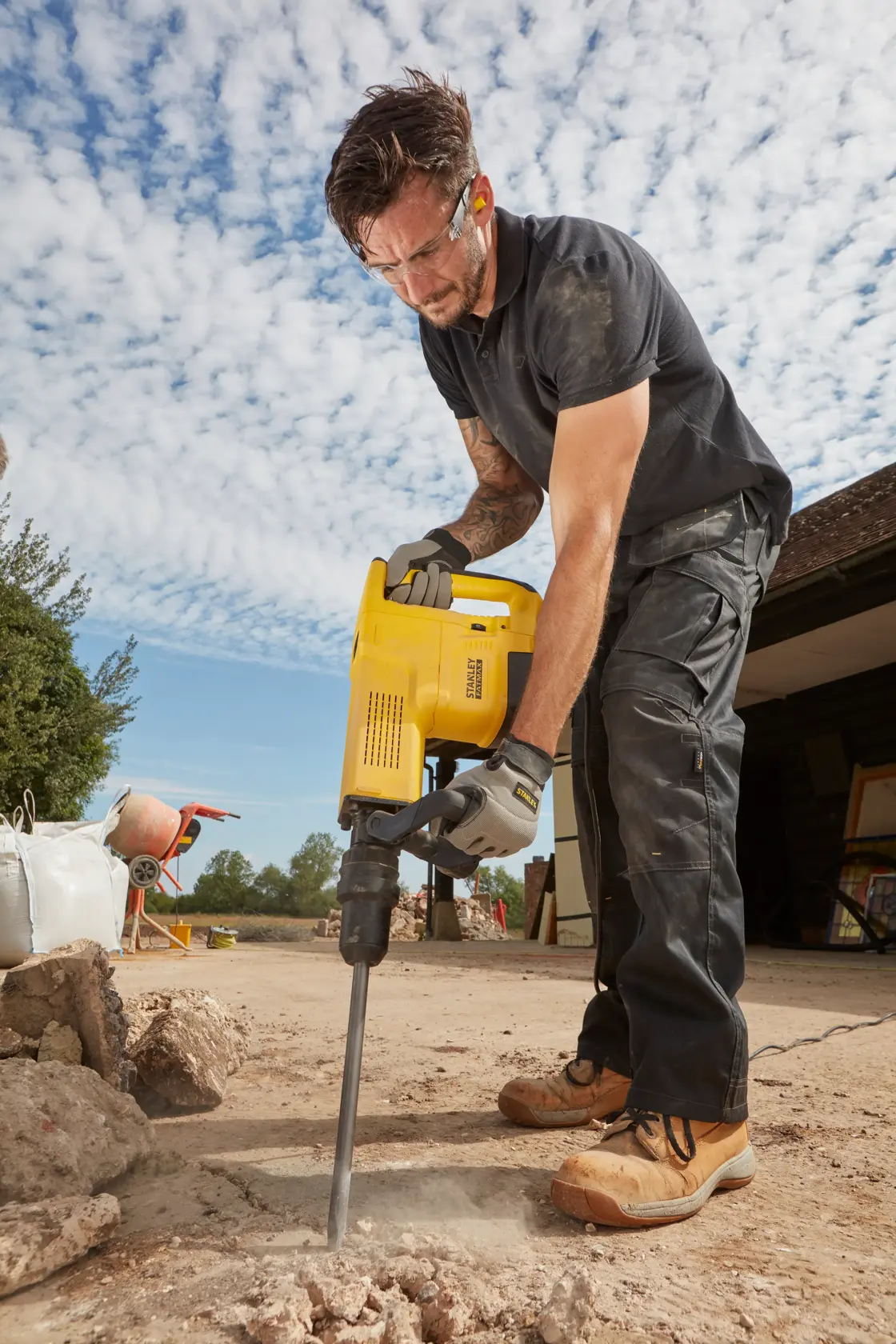 Foto einer Person mit STANLEY SFMEH230K-QS Abbruchhammer auf Außenbeton, Bauszene im Hintergrund.