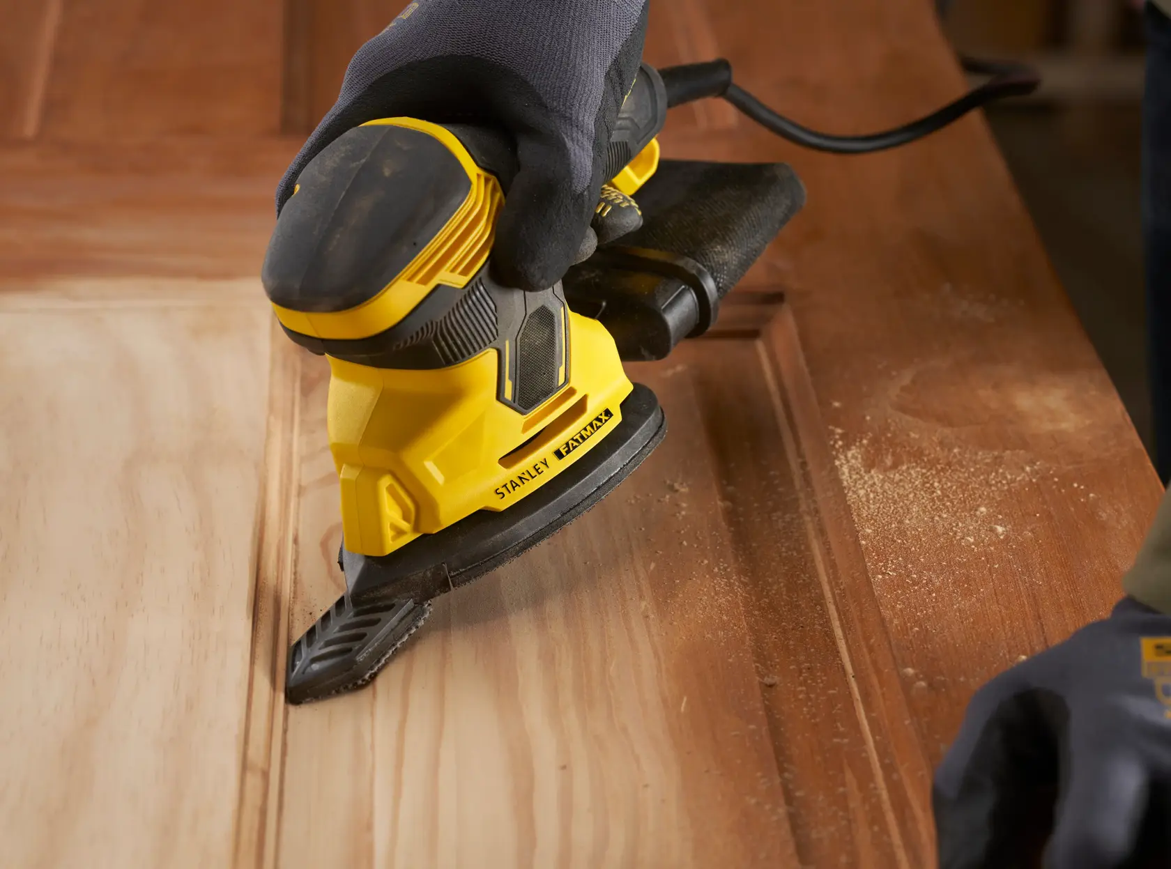 Foto der STANLEY SFMEW210S Schleifmaschine im Einsatz auf Holz, Nahaufnahme mit Staub und ergonomischem Design.