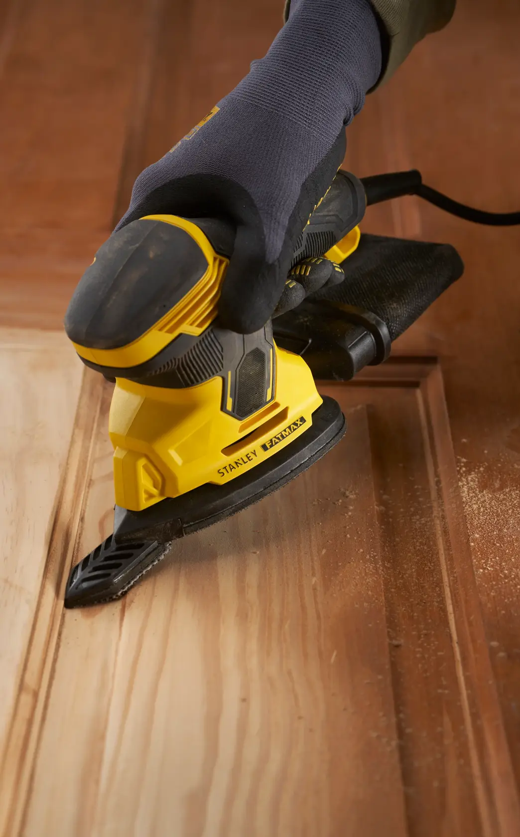 Stanley SFMEW210S Schleifer, gelb und schwarz, im Einsatz auf Holz, Nahaufnahme aus einem Winkel.