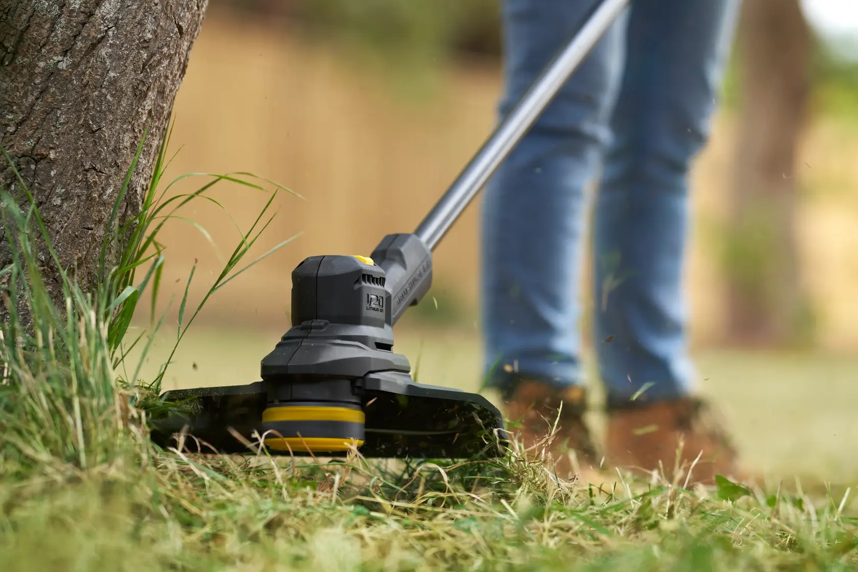 STANLEY SFMSTB930M Rasentrimmer Nahaufnahme im Einsatz, schneidet Gras um einen Baum im Garten.