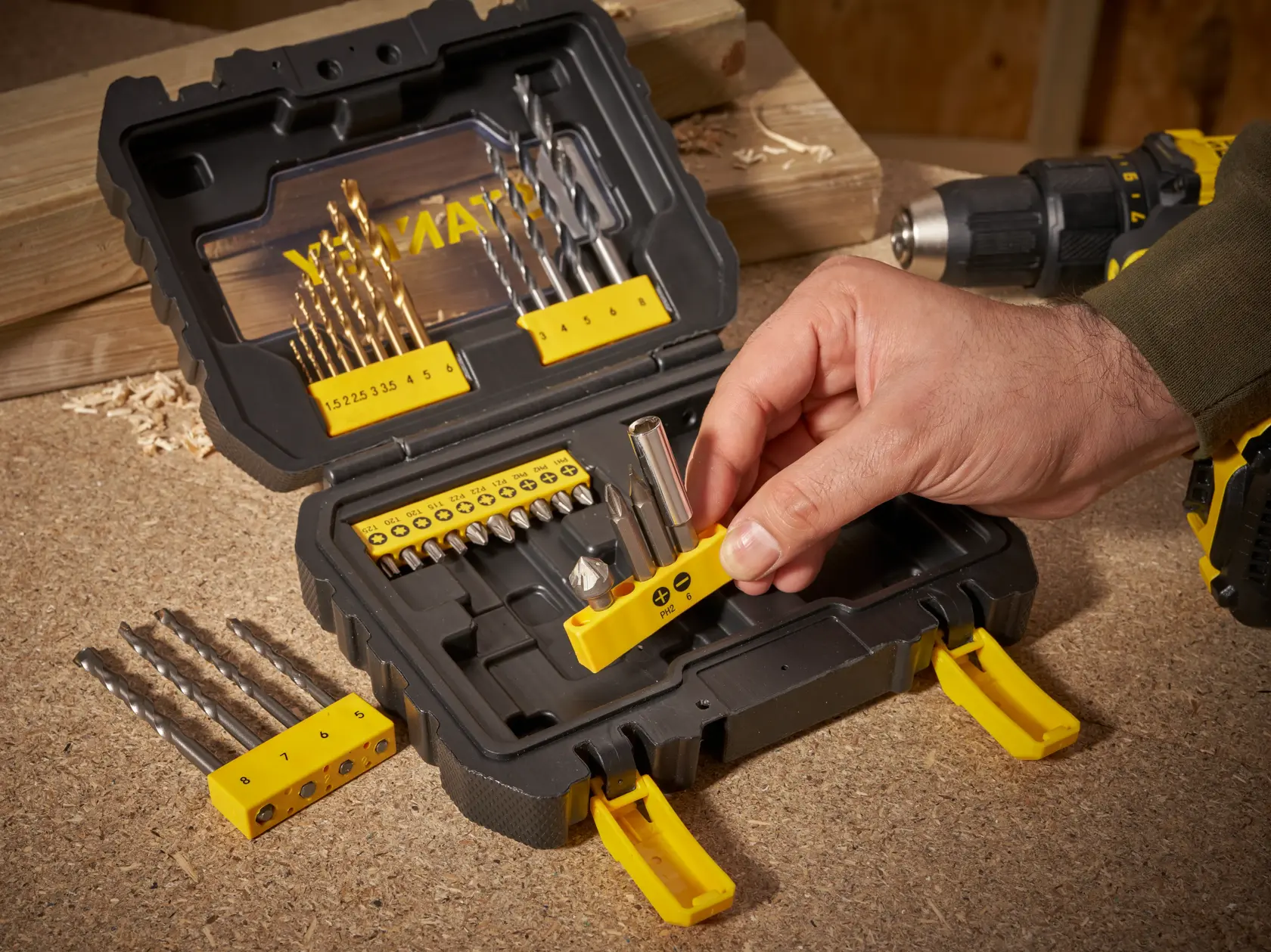 STANLEY STA88550 Bohrer- und Bit-Set auf Werkbank, Hand wählt Bit-Halter aus, Foto von oben.