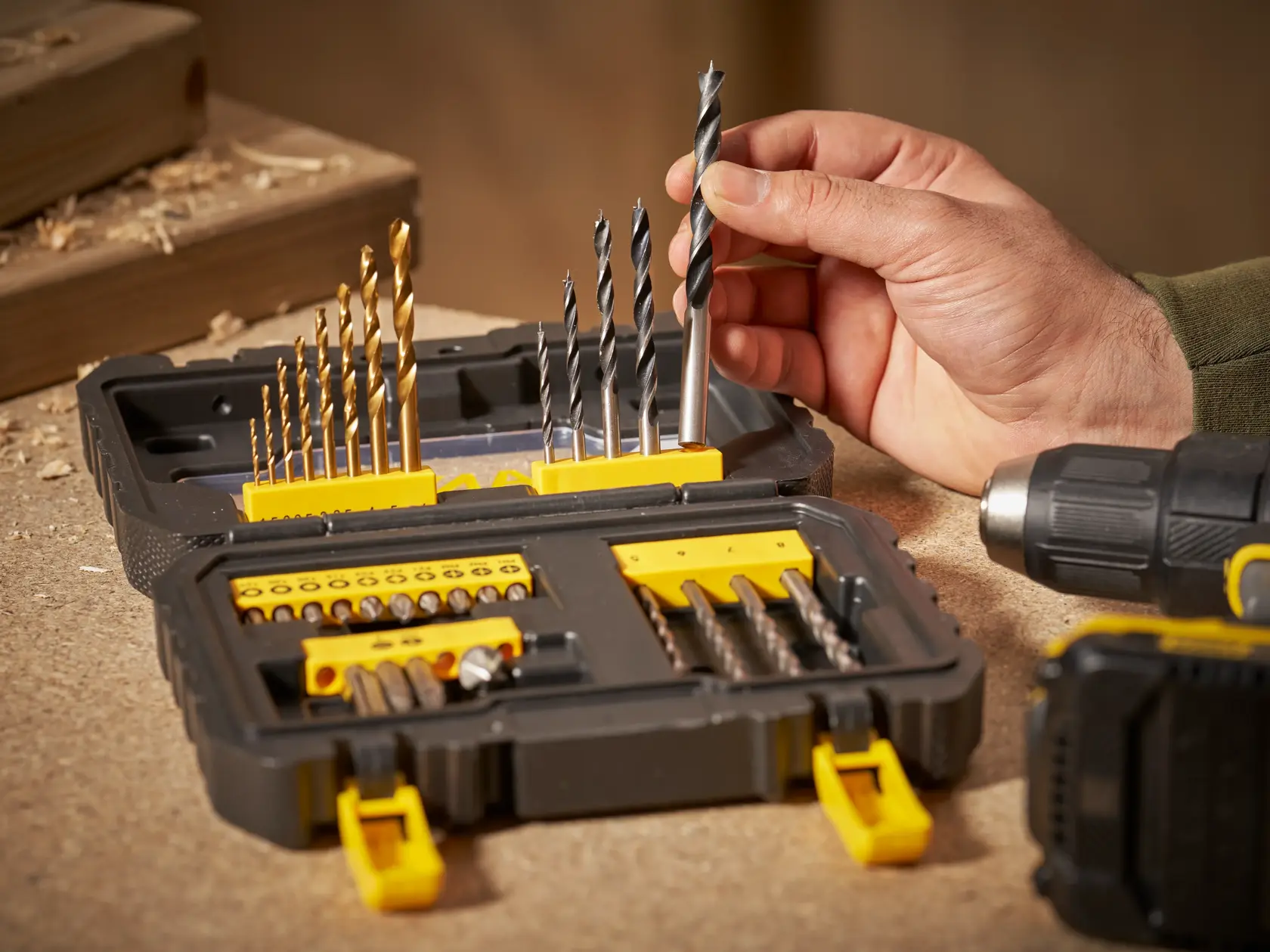 STANLEY STA88550 Bohrer- und Zubehörset offen auf Werkbank, Hand wählt einen Bohrer, Seitenansicht.