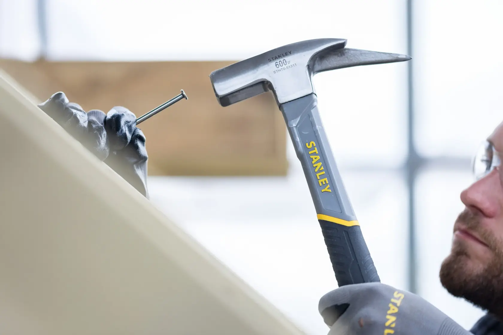STANLEY STHT0-51311 Hammer im Einsatz, schlägt auf einen von einer behandschuhten Hand gehaltenen Nagel, Nahaufnahme.